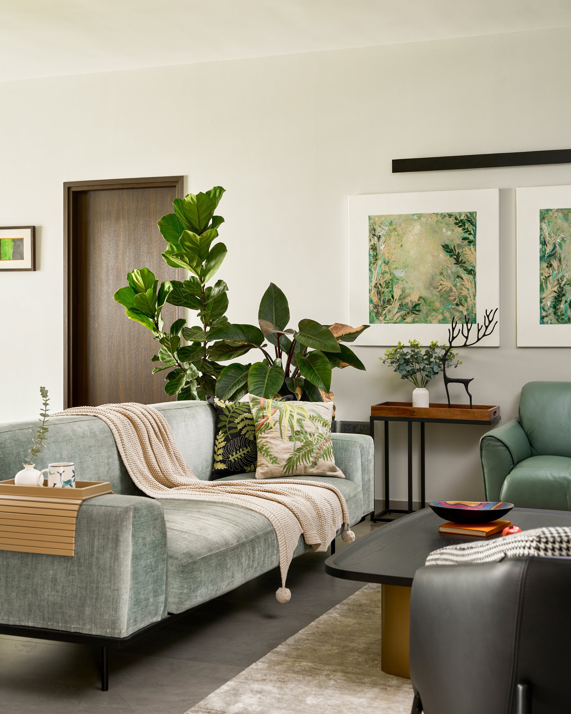 The living room's sage upholstered sofa and leather armchair, where the home's botanical register first announces itself