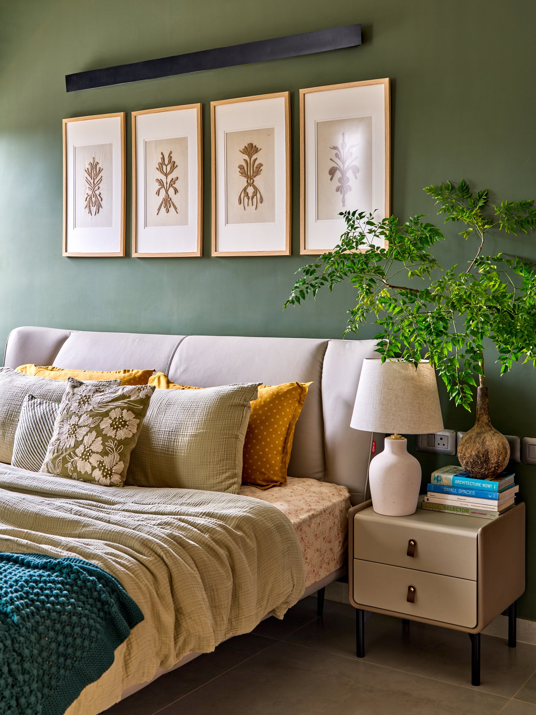 The headboard wall at closer range, where framed botanicals and an upholstered side table soften the green envelope