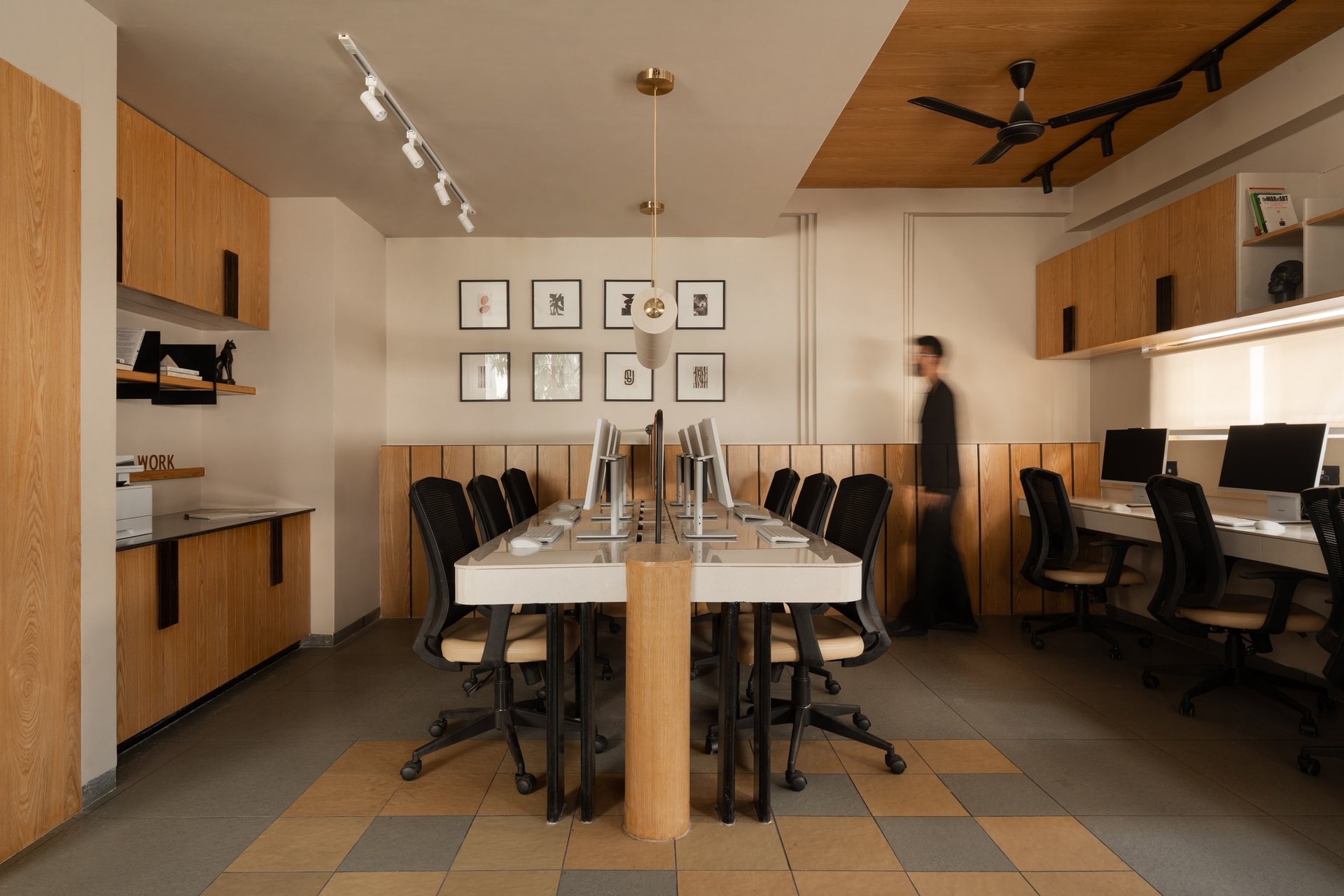 The same workspace seen from the opposite end, where a printer counter and a secondary run of desks along the window edge complete the layout
