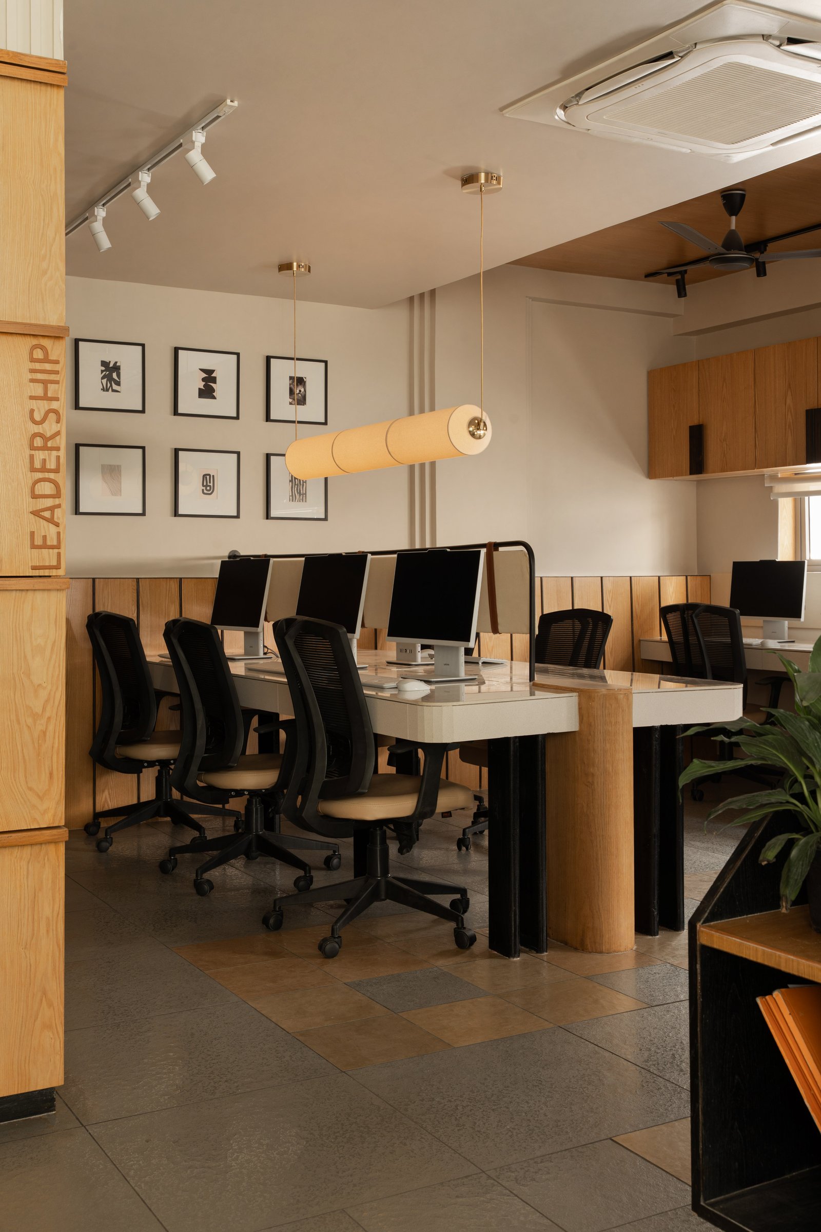 The first-floor workspace, anchored by a central worktable beneath a cylindrical pendant and a column routed with the word LEADERSHIP