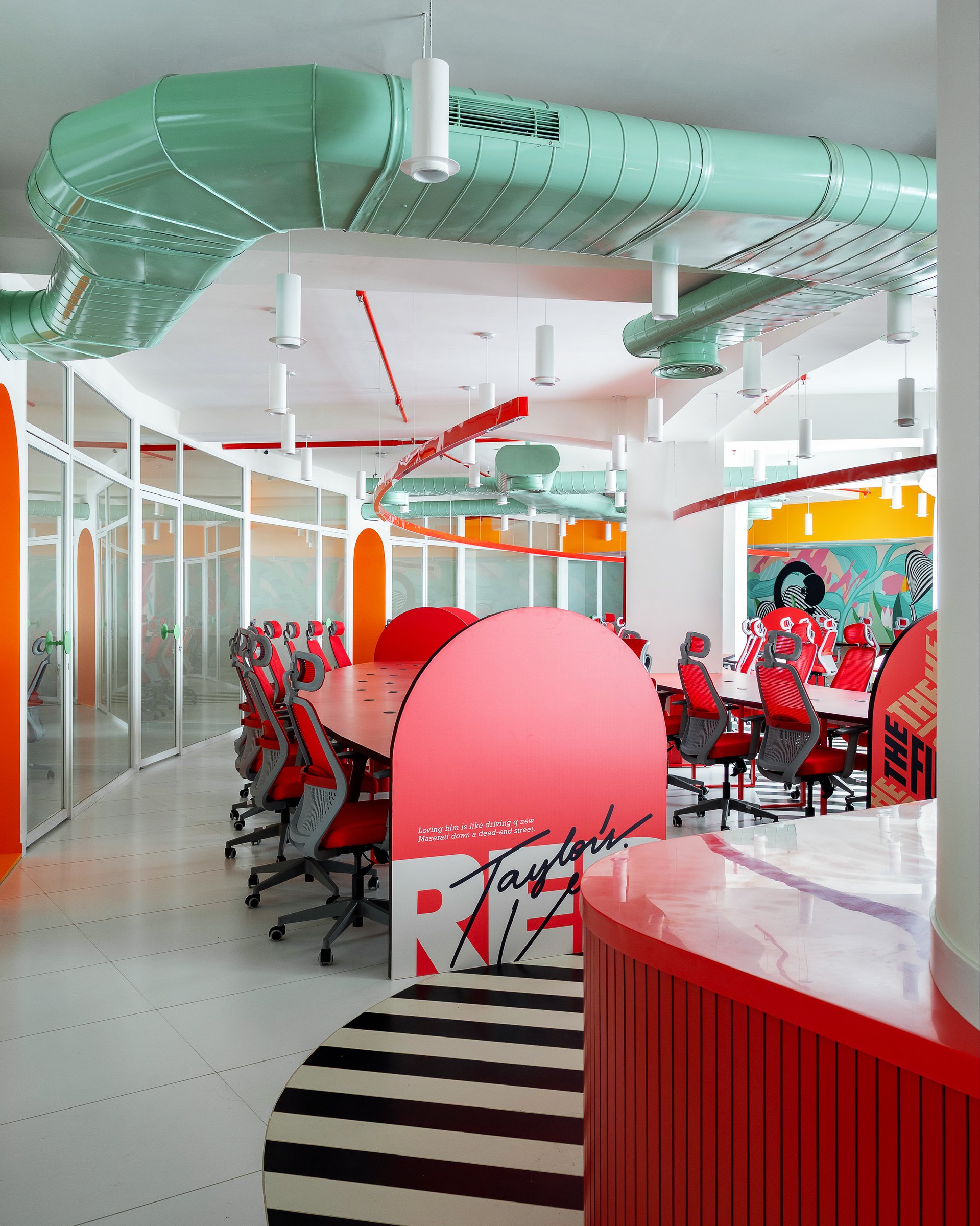 Curved arched dividers in coral introduce graphic voice between workstations, sectioning the long bench into smaller cognitive units