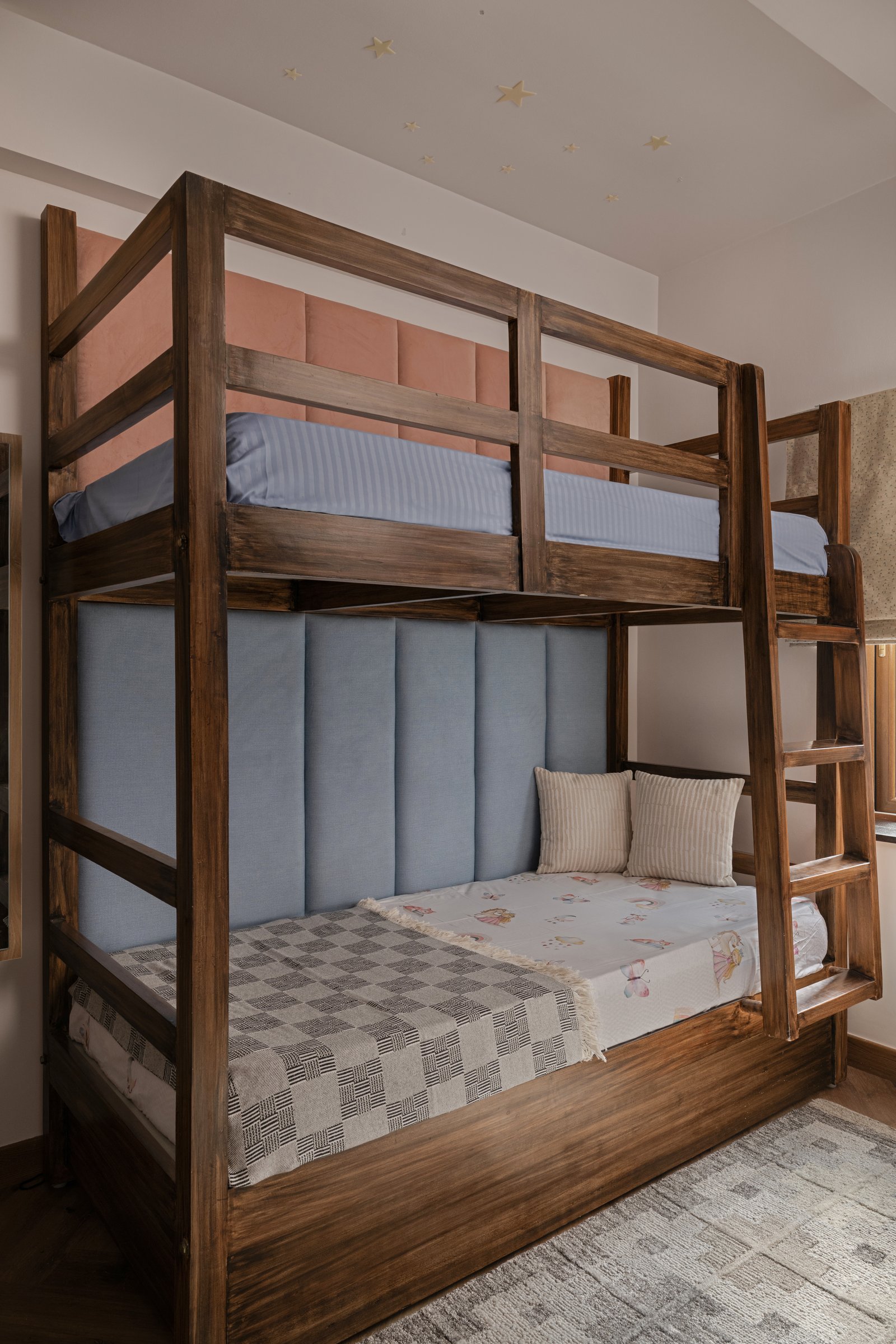The daughters' room, anchored by a solid wood bunk bed with coral and blue upholstered panels under a scatter of small gold stars