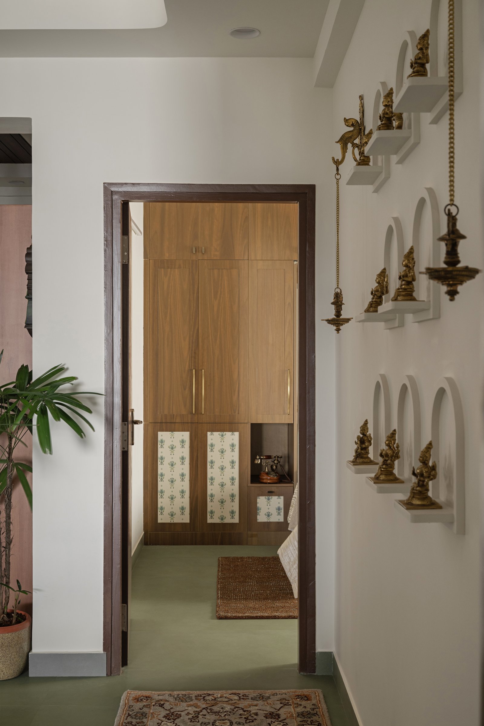 The corridor wall of arched niches holding brass deities, turning circulation into a small daily ritual