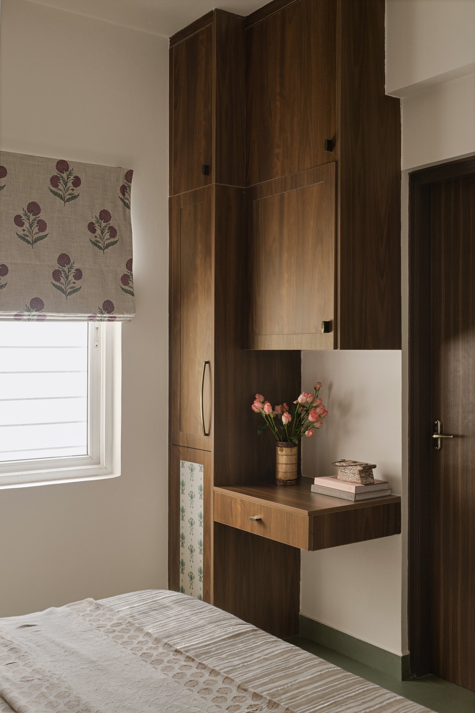 A floating bedside ledge integrated into the wardrobe geometry, with a patterned wallpaper insert hinting at heirloom-saree storage within