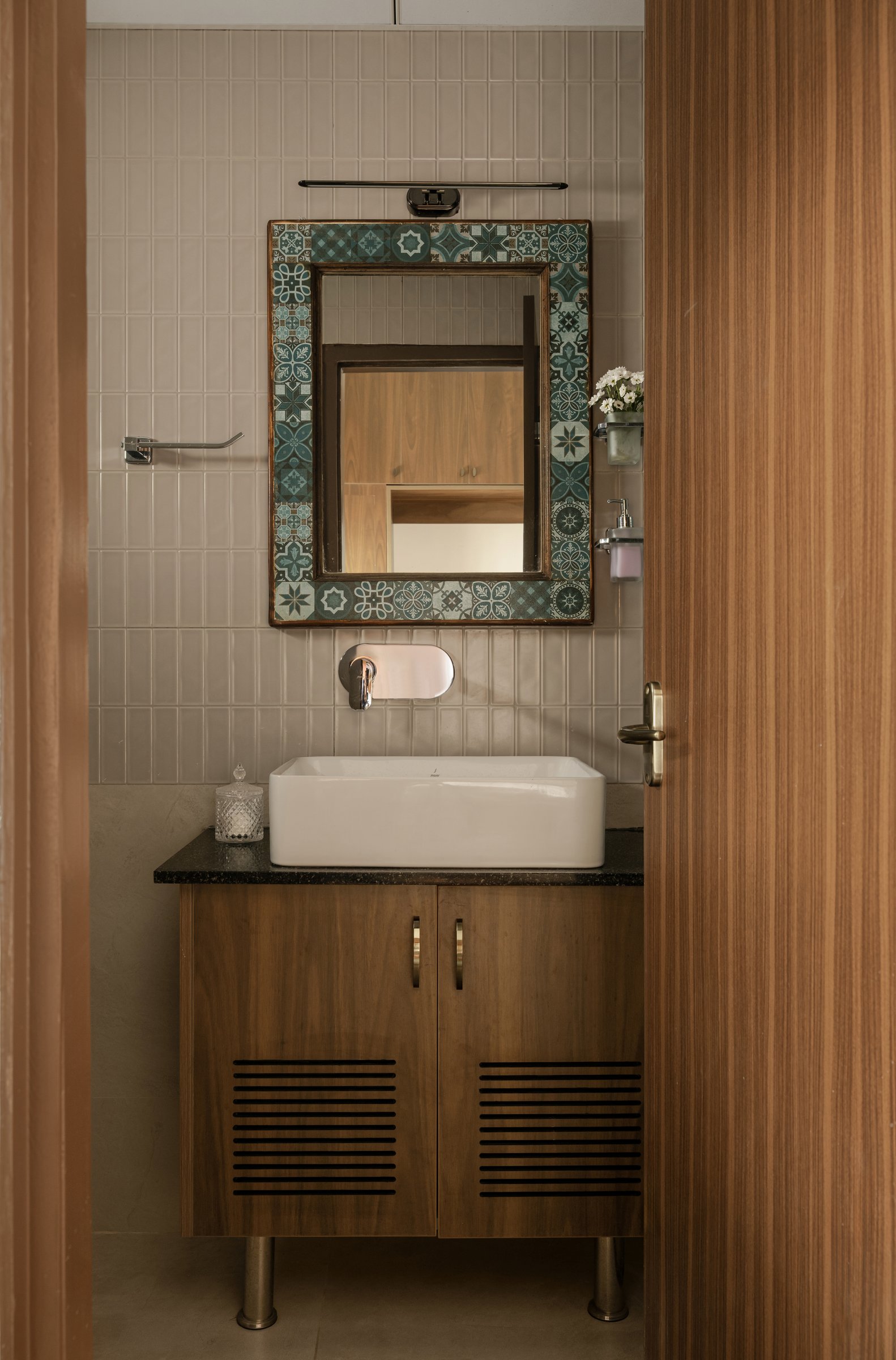 The powder room, where a mosaic-tile mirror border and a slatted wooden vanity sit against a stacked vertical tile wall