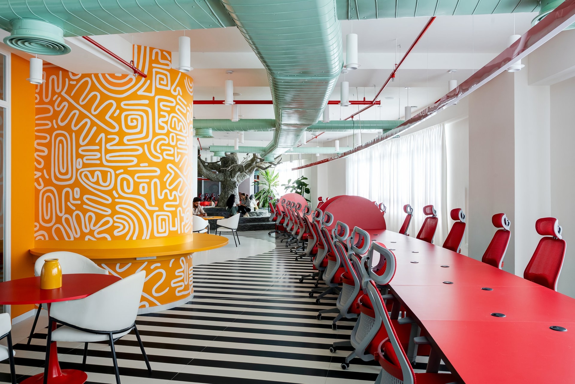 The collaborative spine: a long red working surface running beneath looping mint ducts and a graphic column carrying the orange motif inward