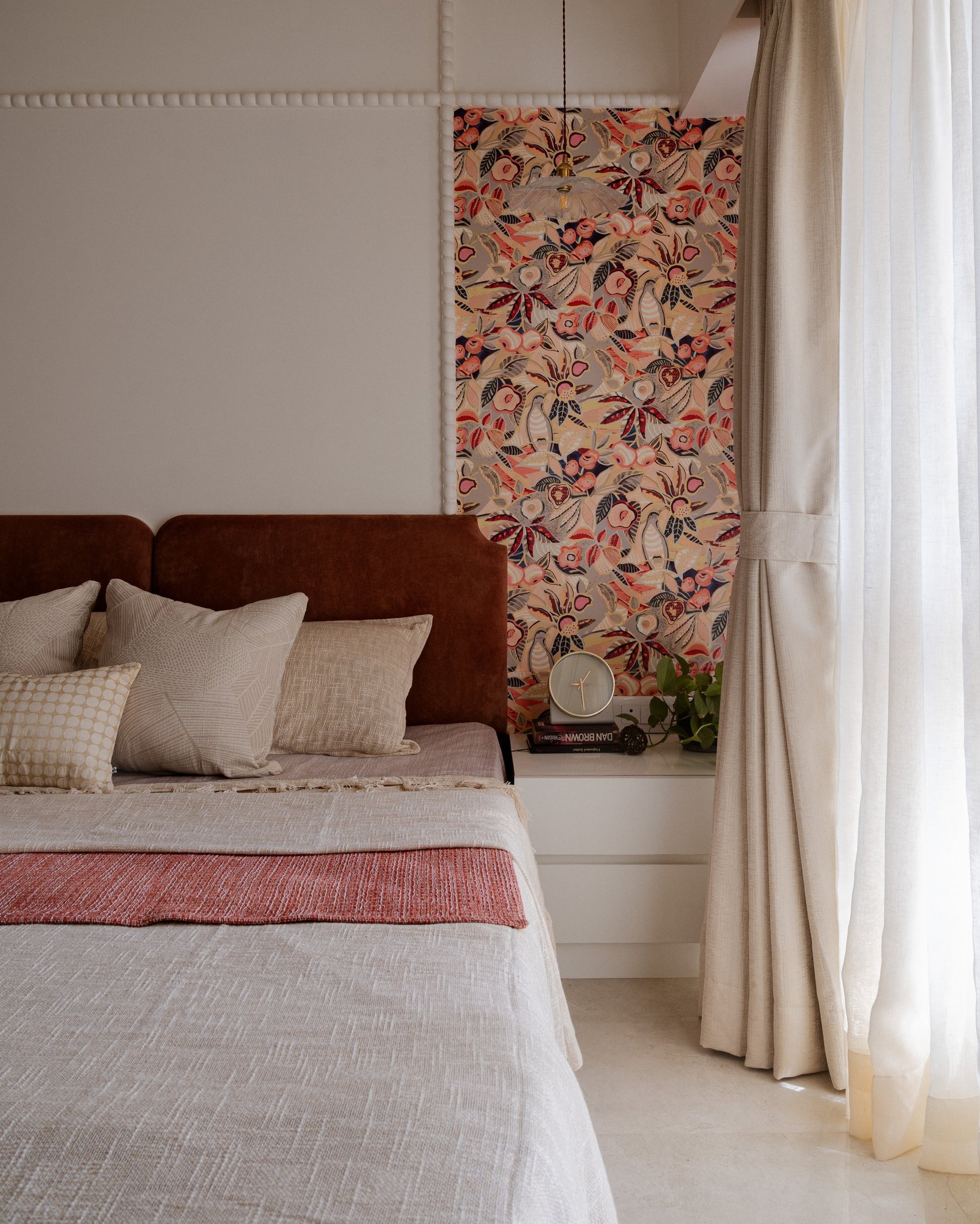 The master bedroom, where a rust velvet headboard and a framed panel of botanical wallpaper hold a single chromatic thought