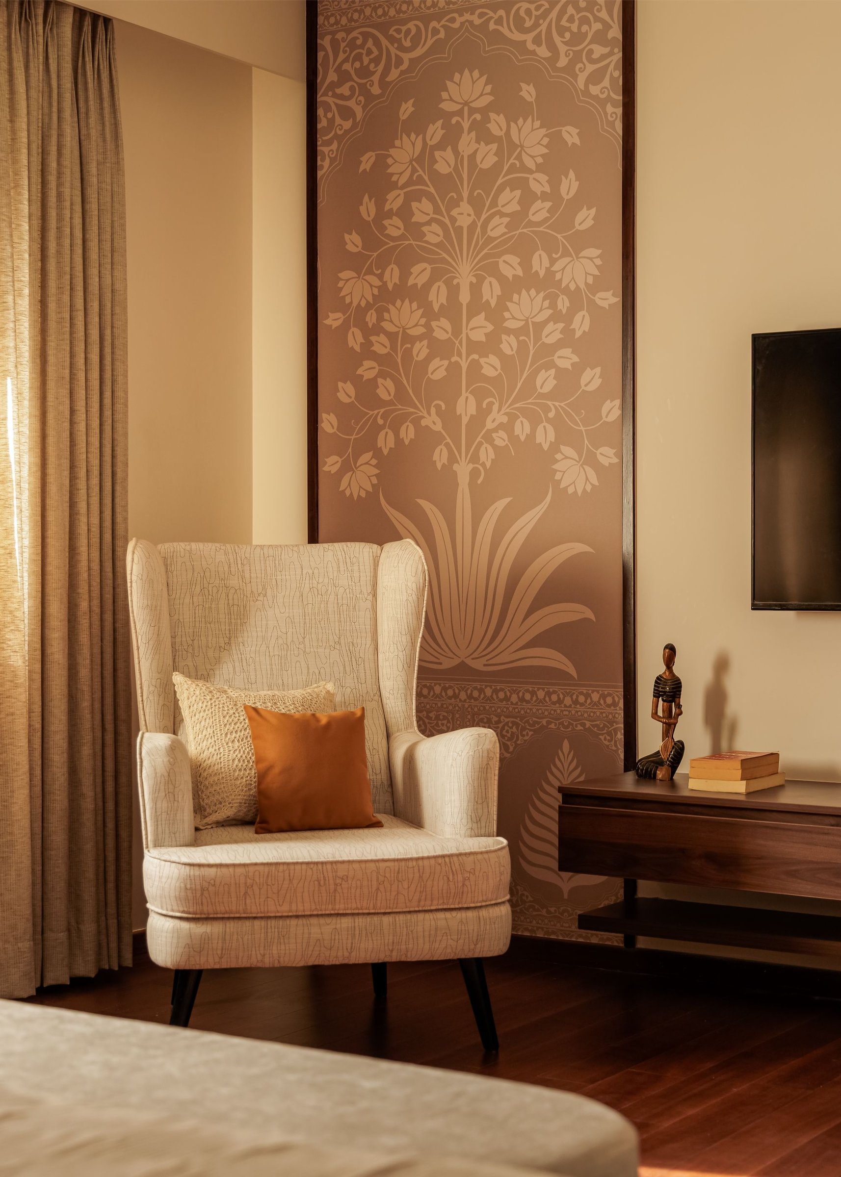 A reading corner where a cream wingback chair sits against a lotus-motif panel