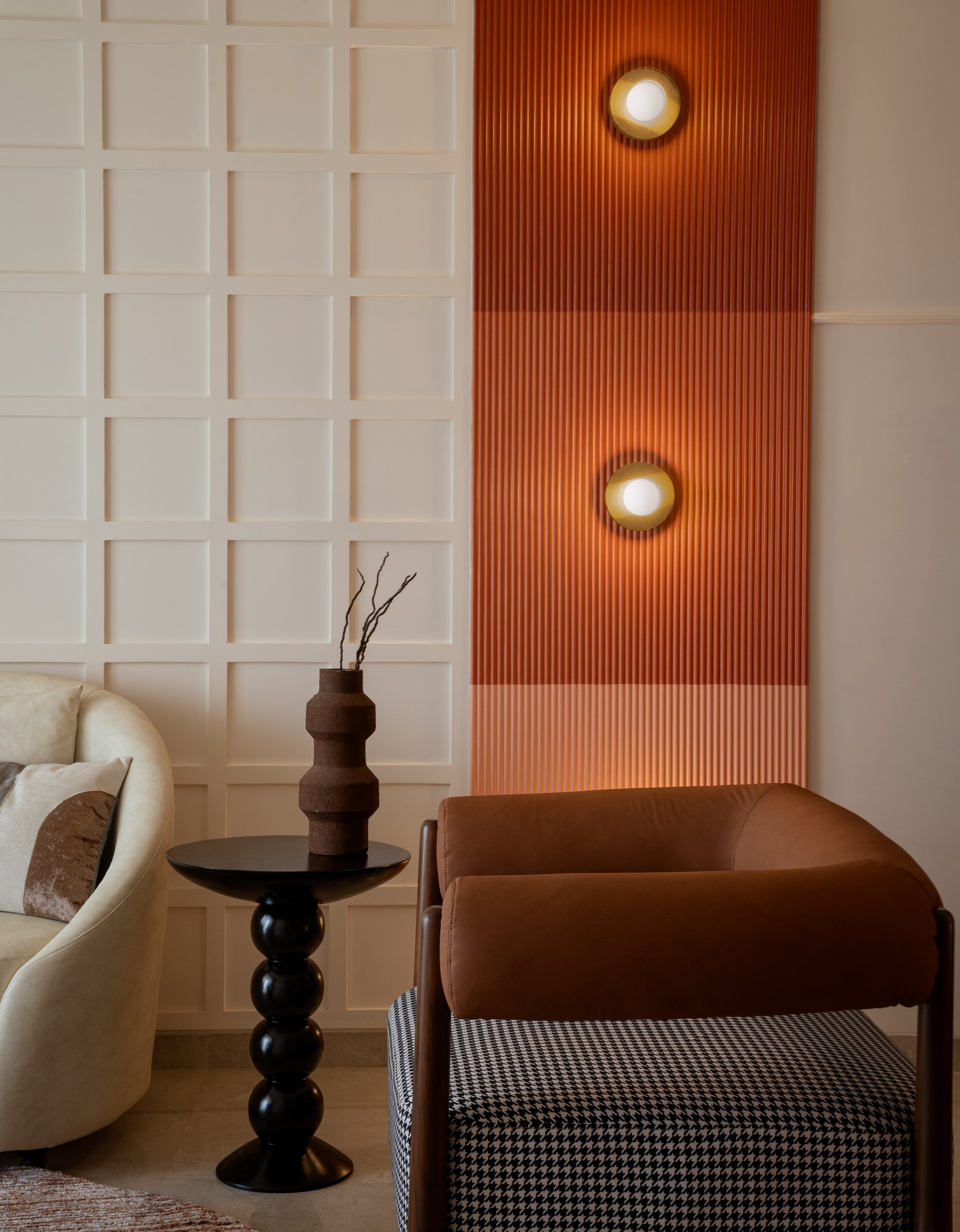 The terracotta fluted plaster panel between the living and dining zones, where a pair of round brass sconces glow against the home's signature gesture