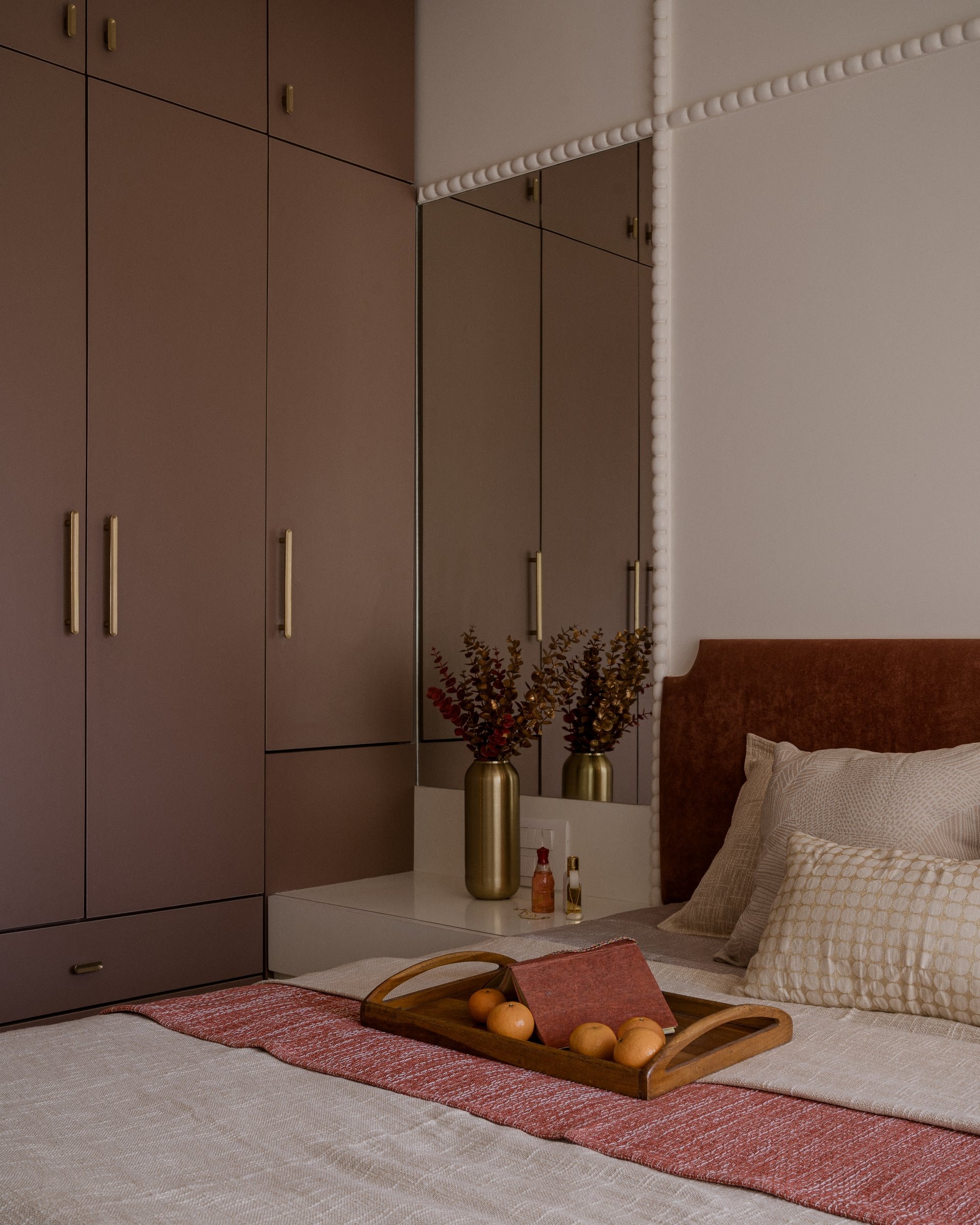 The wardrobe wall, where muted clay-red joinery runs full-height and a mirrored section opens above a dressing ledge