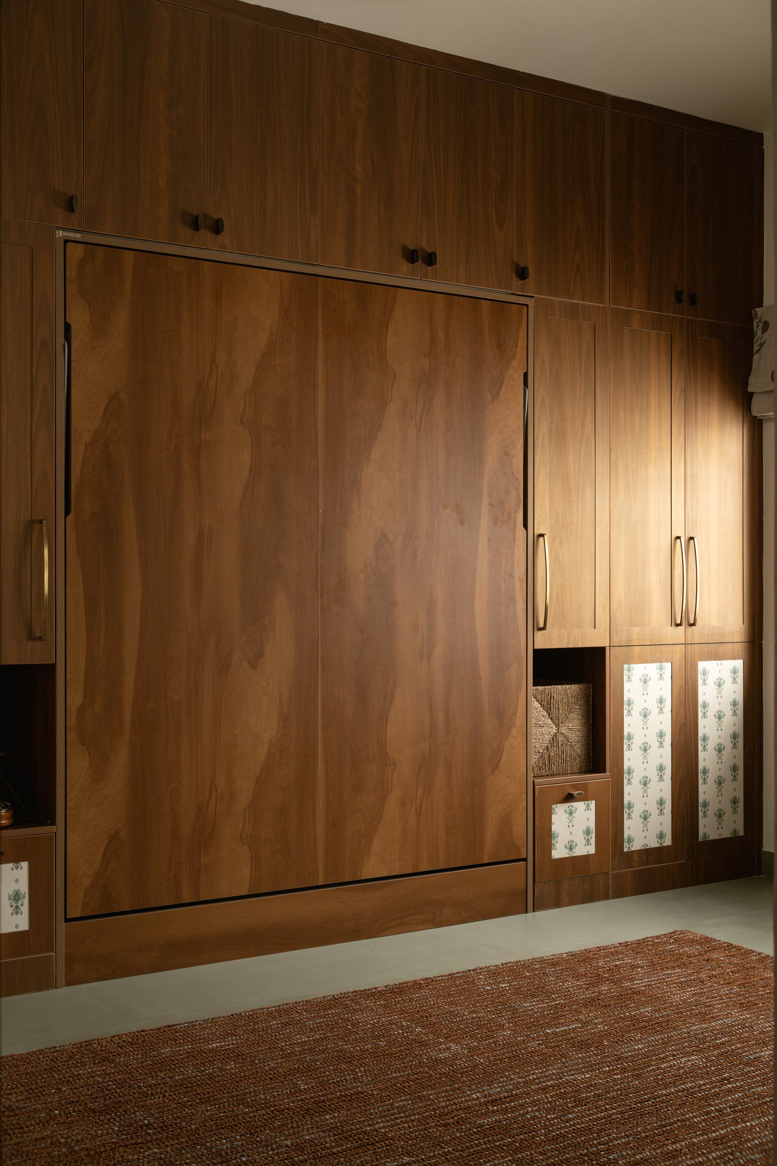 The master's storage wall, where a concealed fold-down bed sits within a full run of warm-toned wardrobes