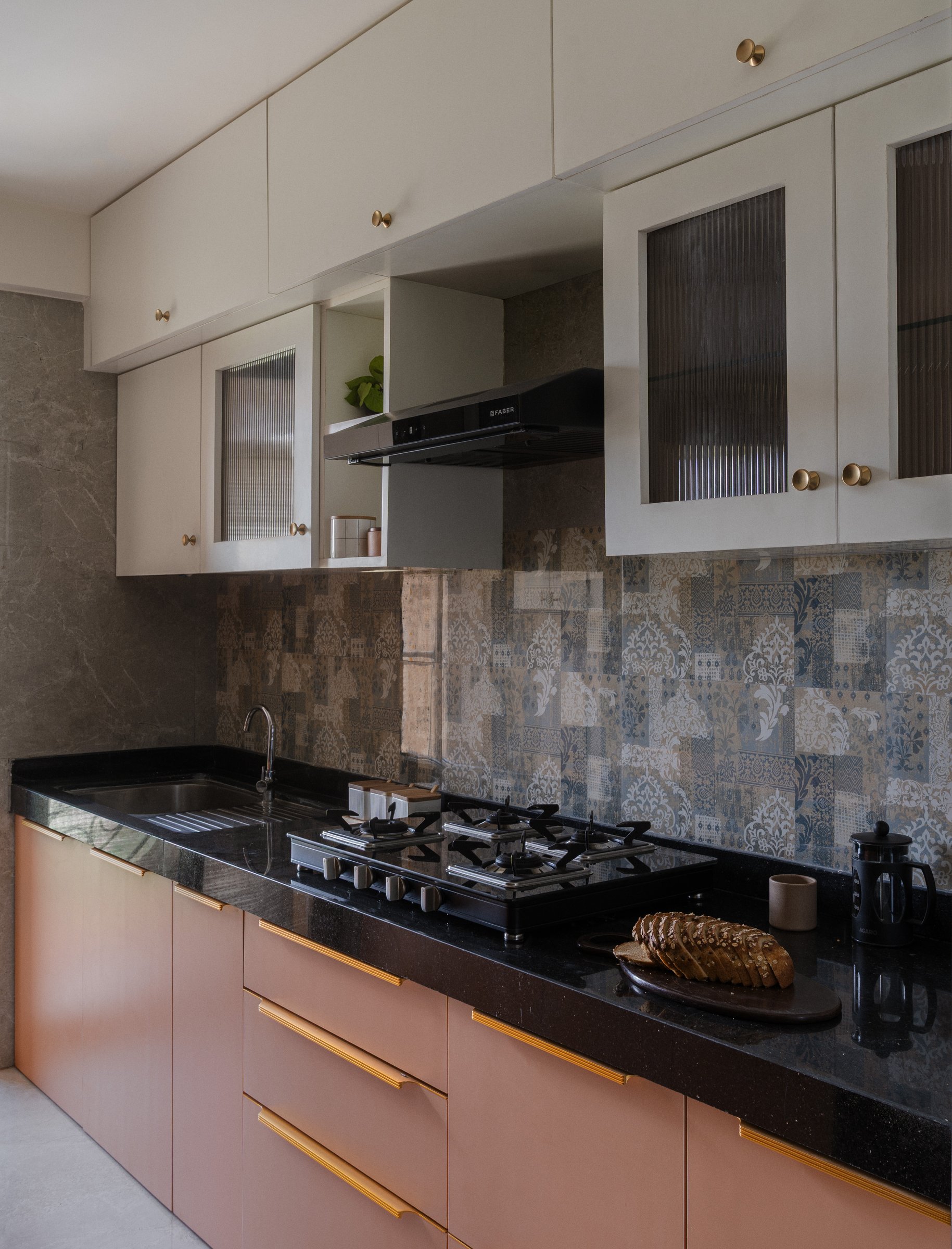 The kitchen, where dusty pink lower cabinets and a patterned backsplash temper the gravity of a black granite worktop