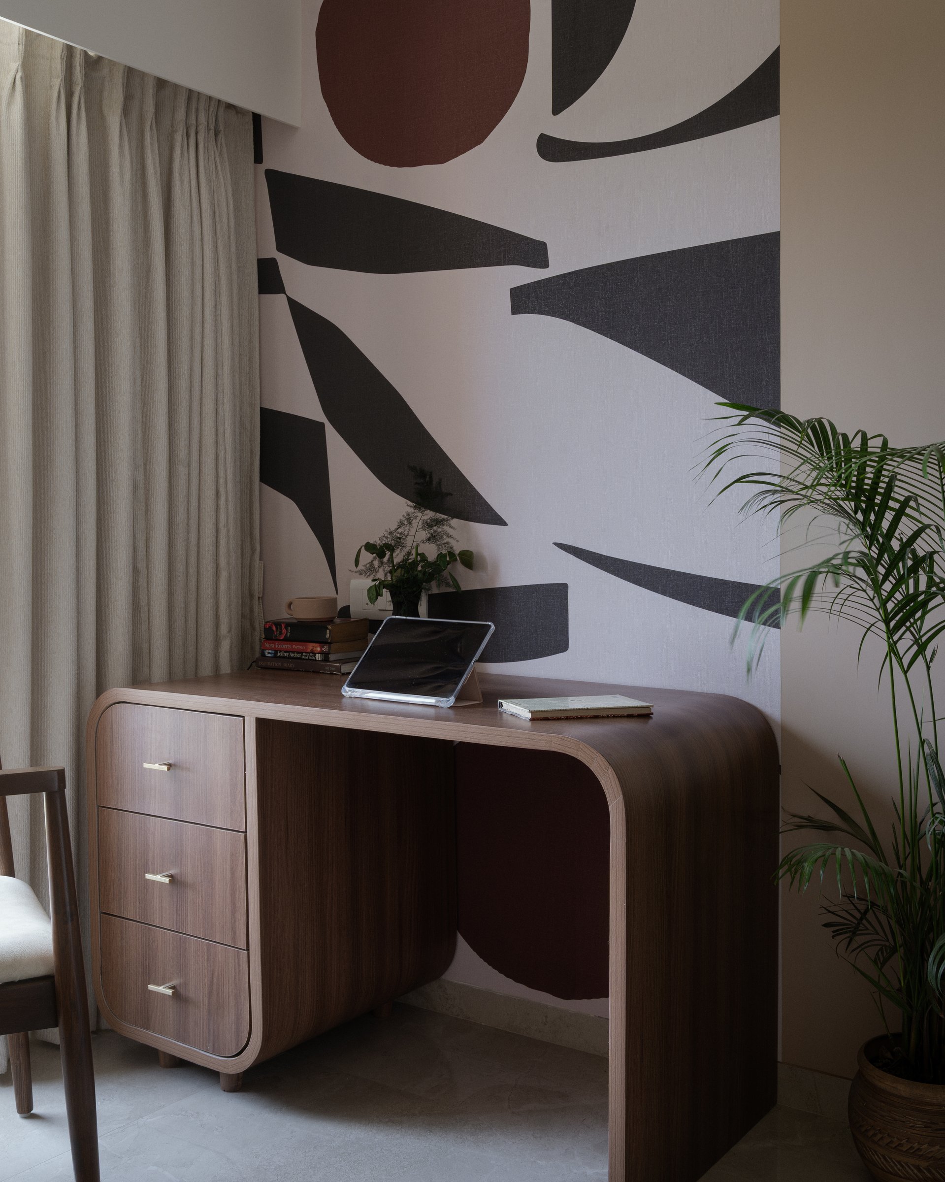 The study corner, where a curved walnut writing desk meets a mural-scale abstract wallpaper