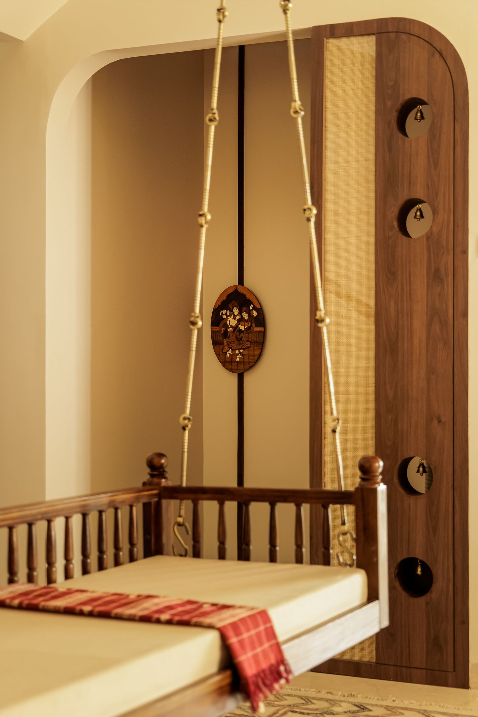The jhula in close view: rope suspension, brass bells set into circular cutouts, and an inlaid wooden medallion behind
