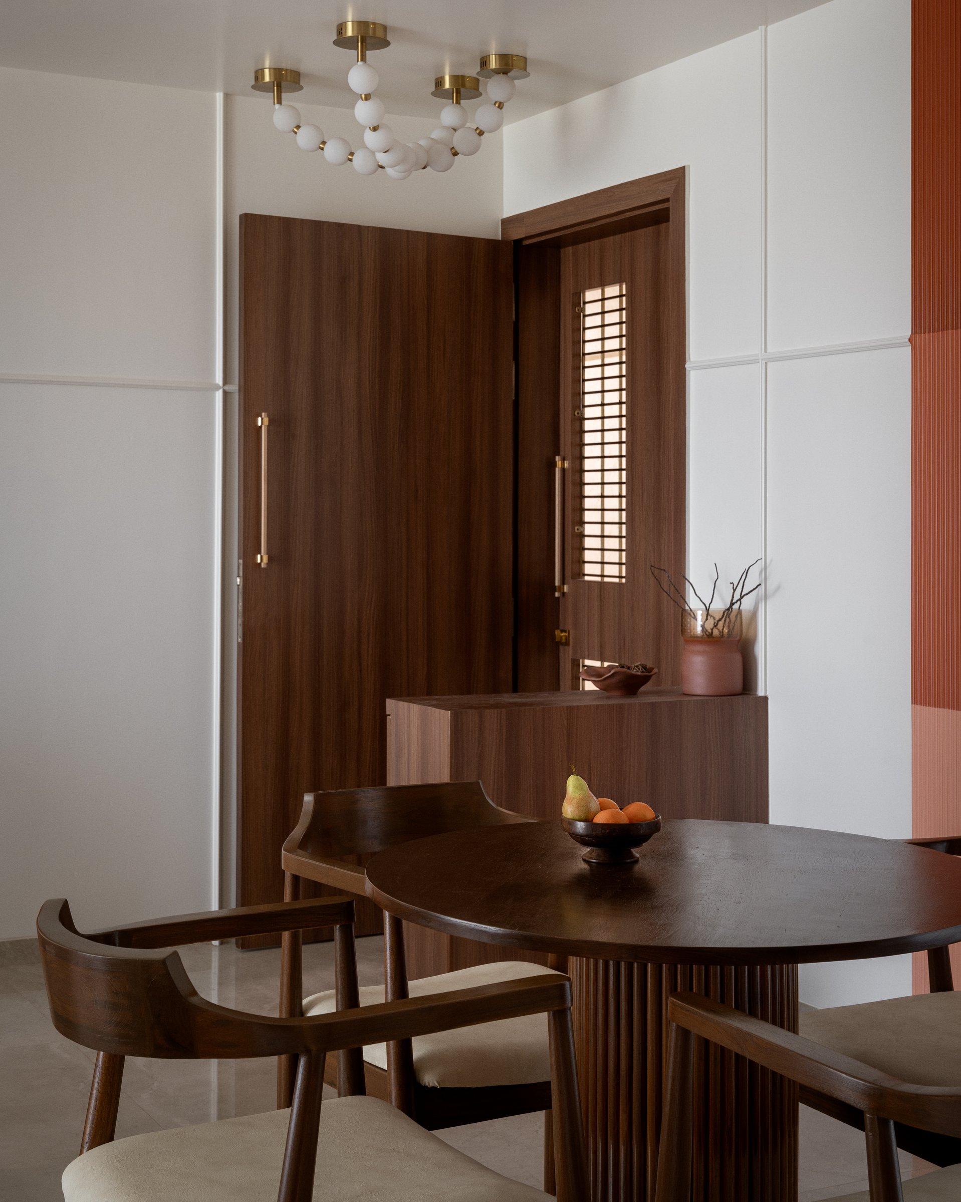 The dining area, where an oval walnut table on a fluted pedestal base sits beneath a beaded glass-globe chandelier