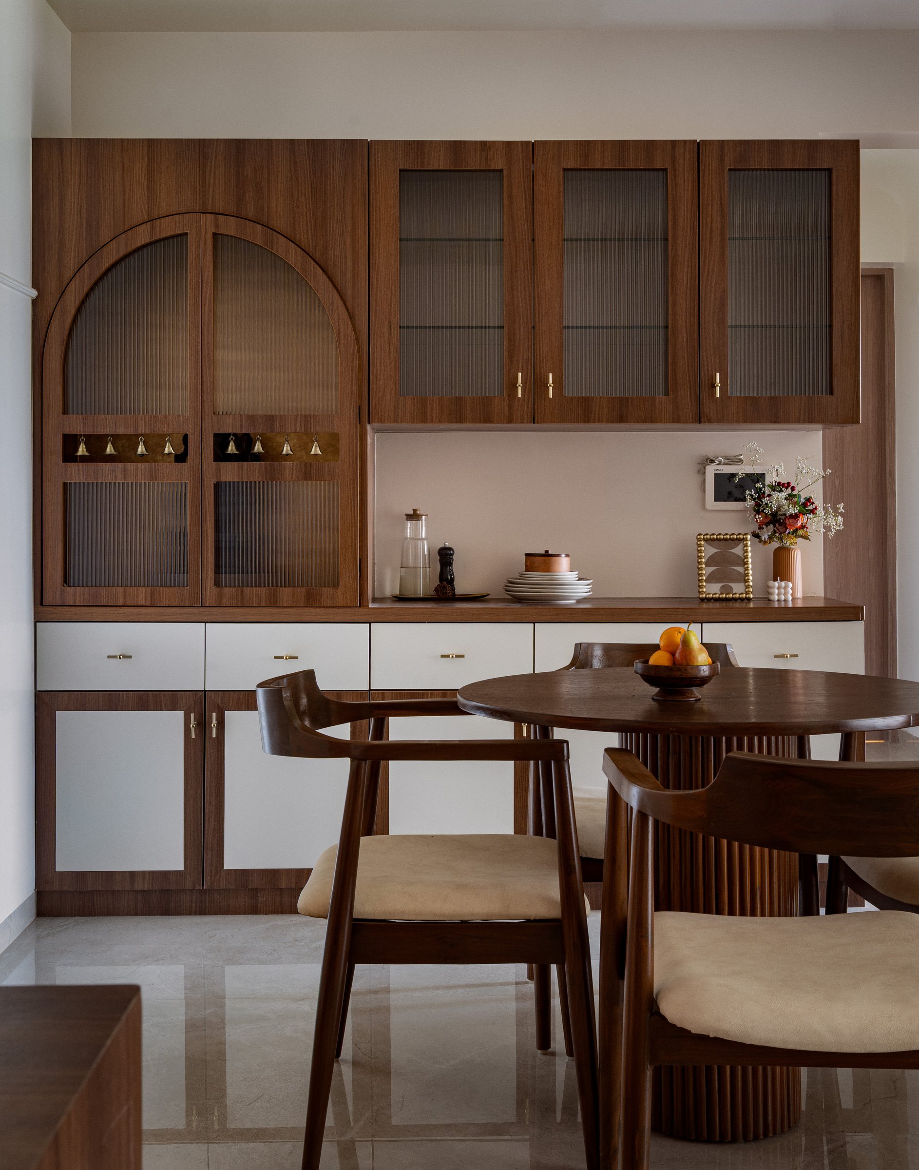 The crockery and mandir unit, where an arched fluted-glass door anchors a wall of walnut and white cabinetry