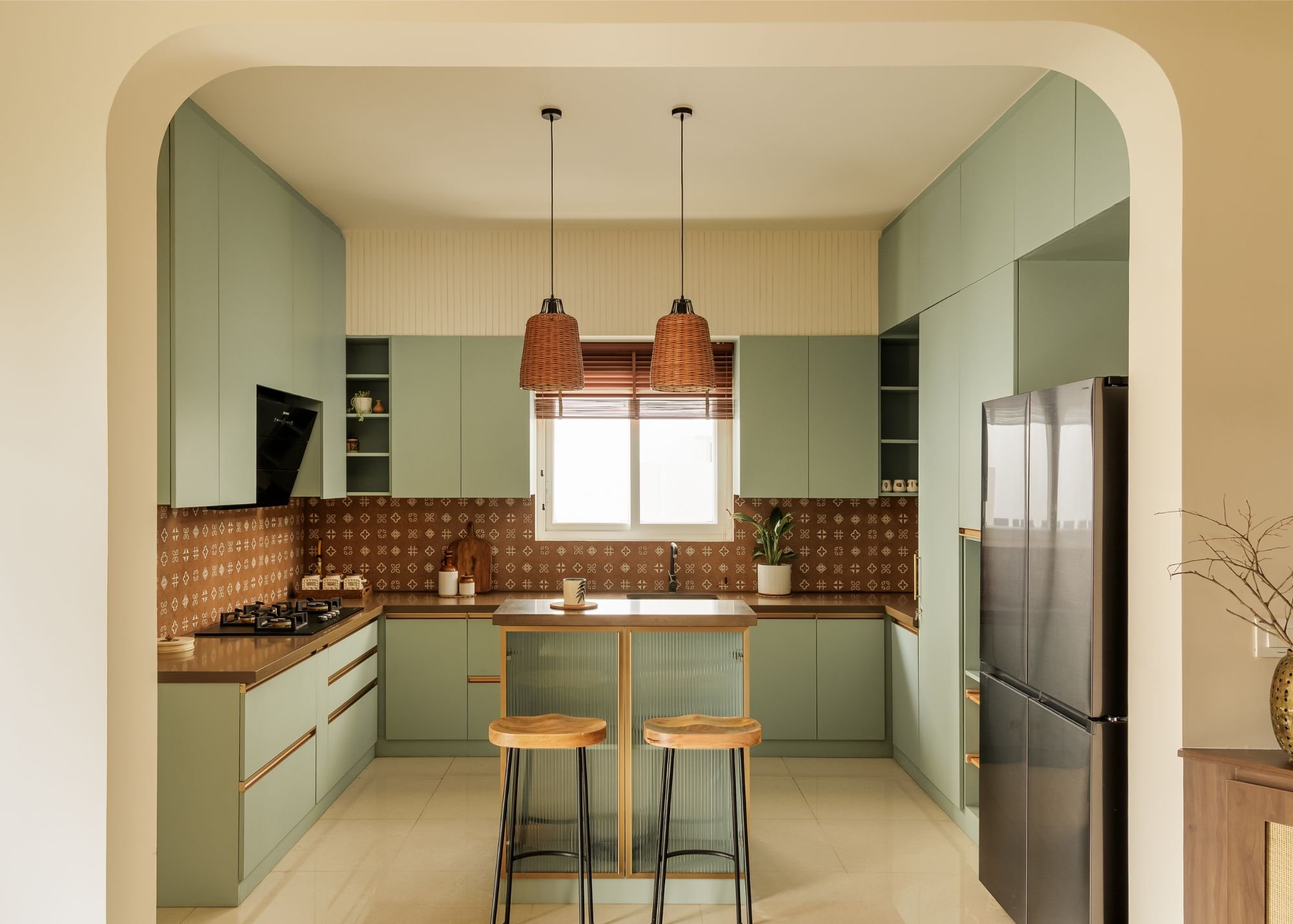 The kitchen, where sage cabinetry meets a patterned terracotta backsplash beneath cane pendants