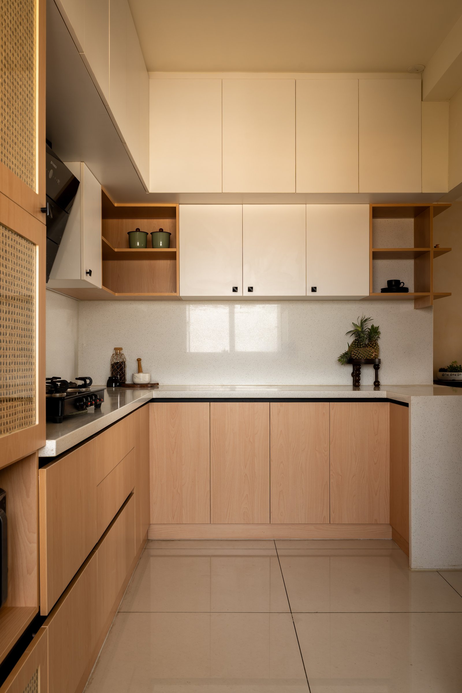 Open shelving and a cane-fronted tall unit keep the kitchen's material vocabulary consistent with the rest of the home
