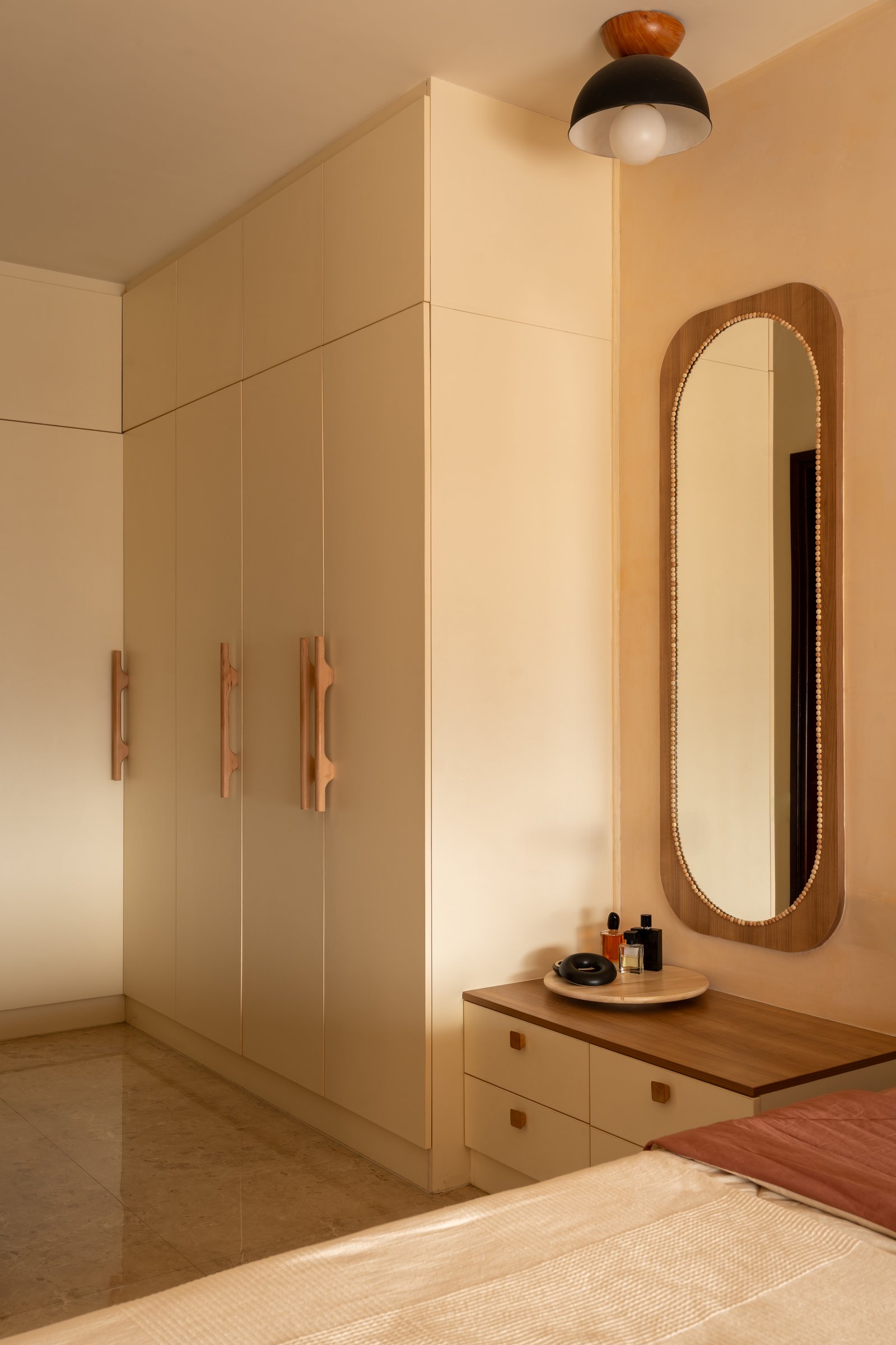 The dressing zone, where a run of cream wardrobes and an oval beaded mirror keep the wall plane quiet