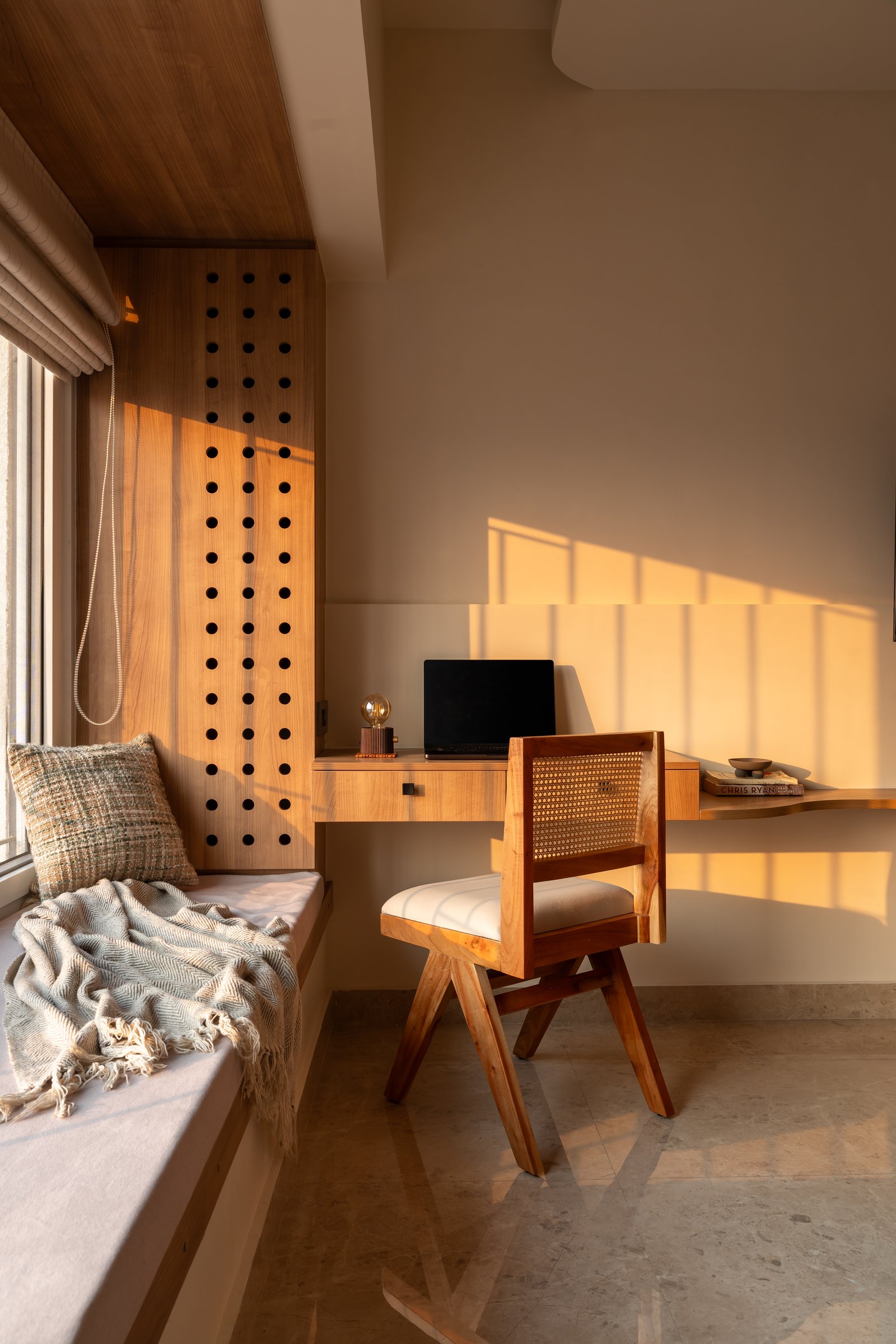 A window-side study with a built-in bench and a perforated wood panel that filters afternoon light into a grid of shadow
