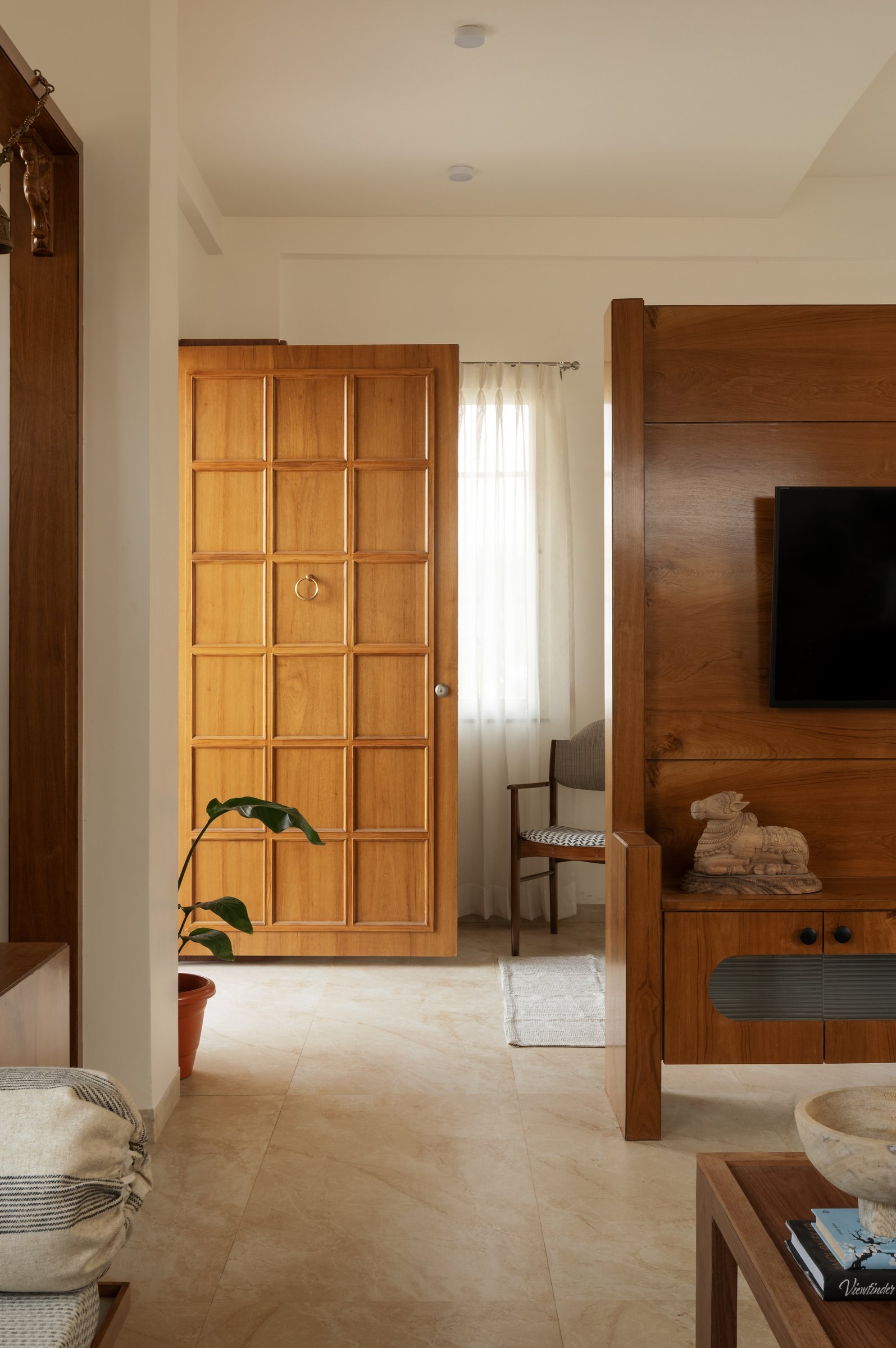 The foyer: a coffered wooden door and a low media unit carrying a small Nandi carving establish the home's material grammar before the rooms truly begin