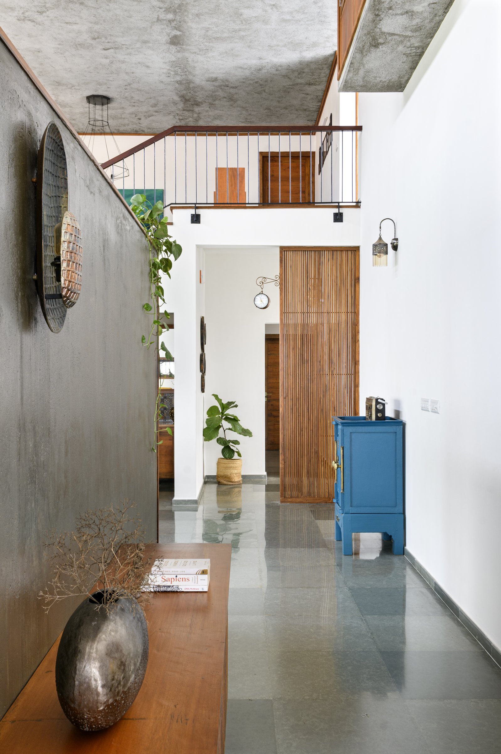 The foyer corridor between a textured concrete wall and a long polished kadappa floor