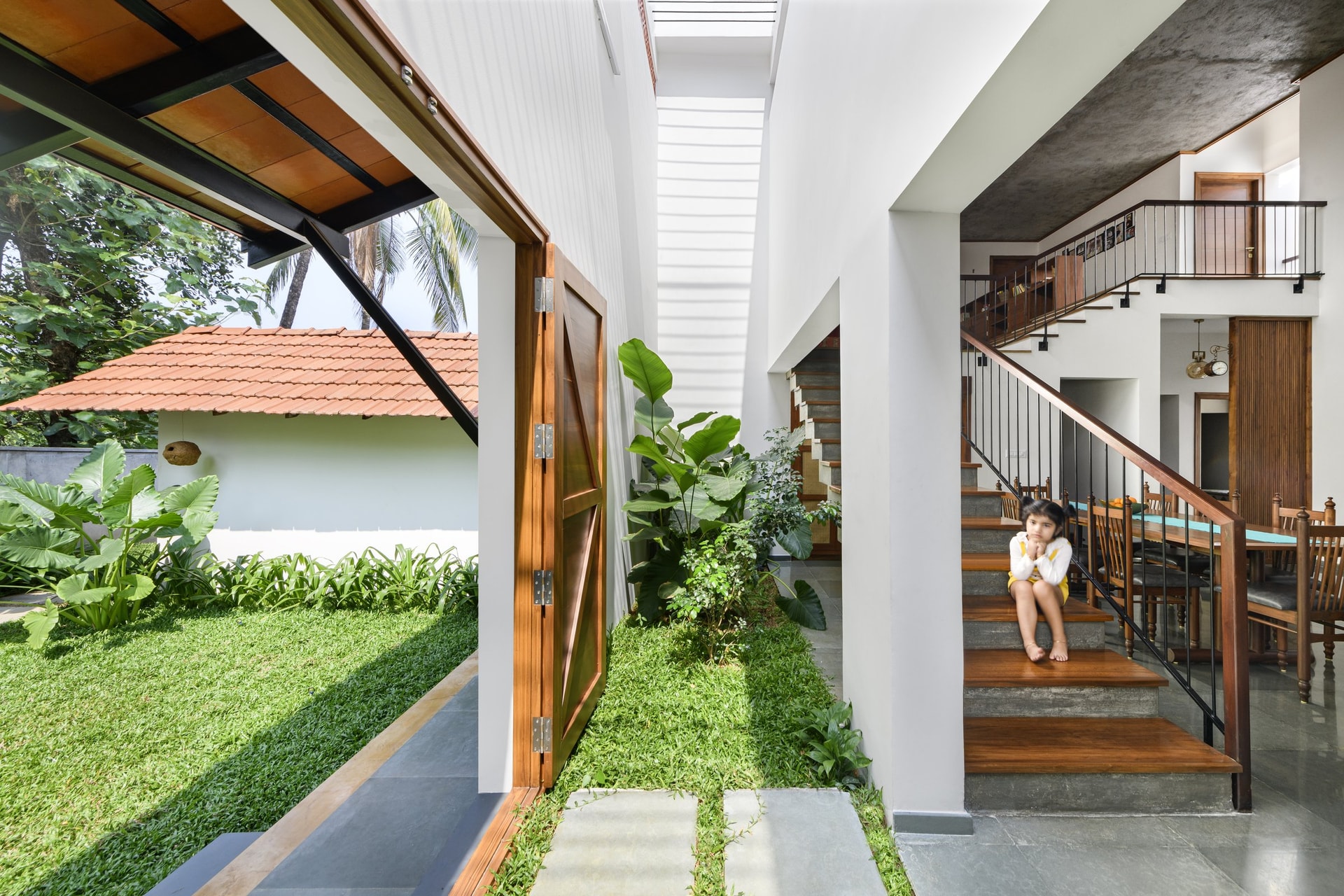 The pivoting entry door opening onto a planted strip beside the staircase, dissolving the threshold