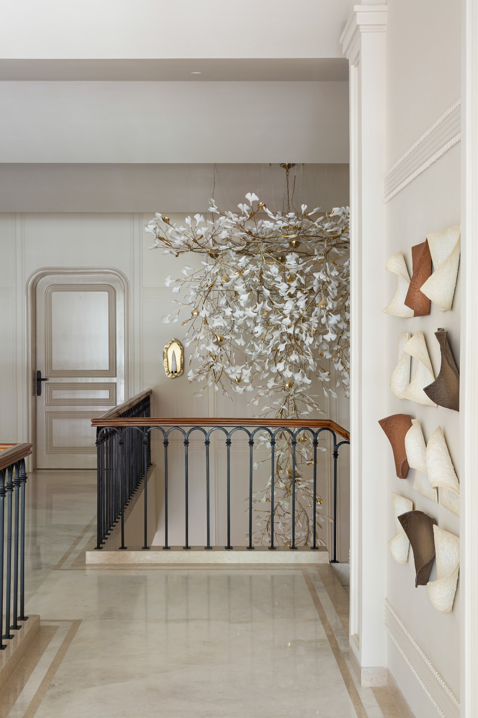 The first-floor landing, where a second porcelain-and-brass chandelier cascades into the double-height void