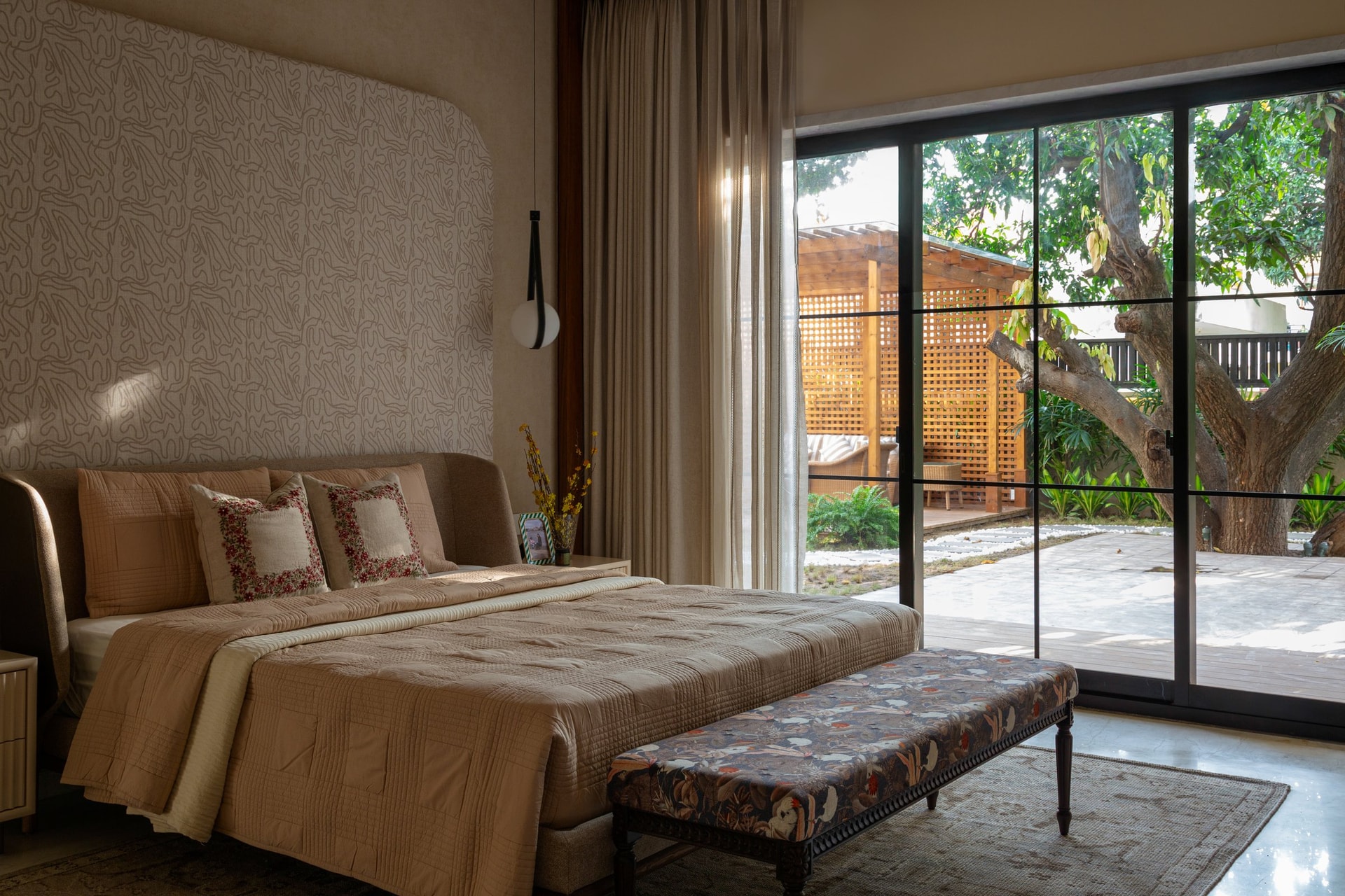 A guest room with a direct relationship to the landscape: oat tones inside, the mature tree just beyond the glass