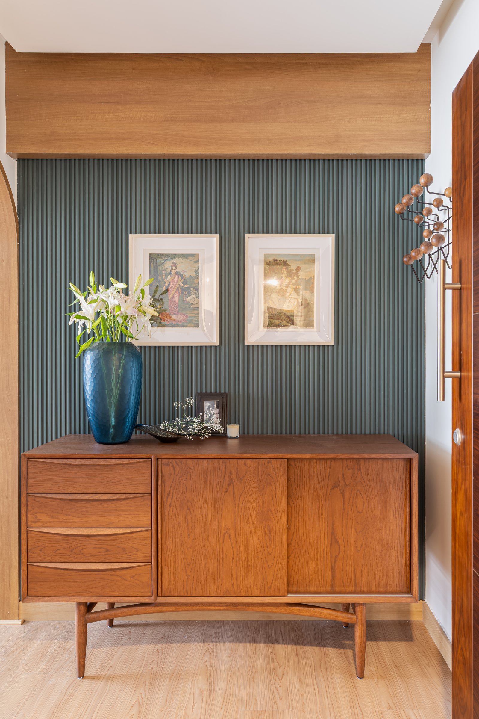 The foyer, where a teak sideboard and fluted olive panel set the home's material grammar before any room is entered