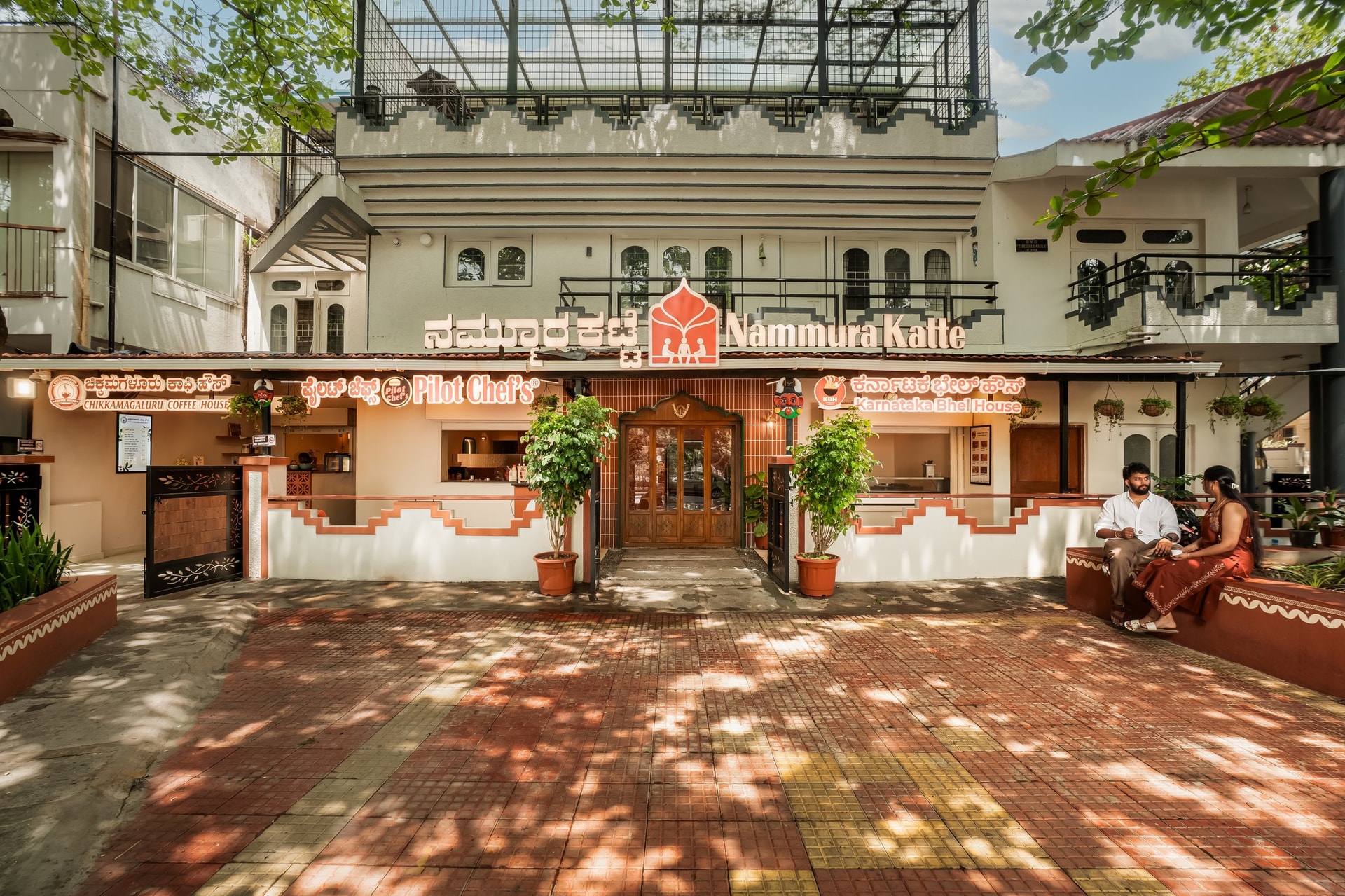 The street frontage, where three vendor identities share a single terracotta-toned elevation set back behind a shaded forecourt