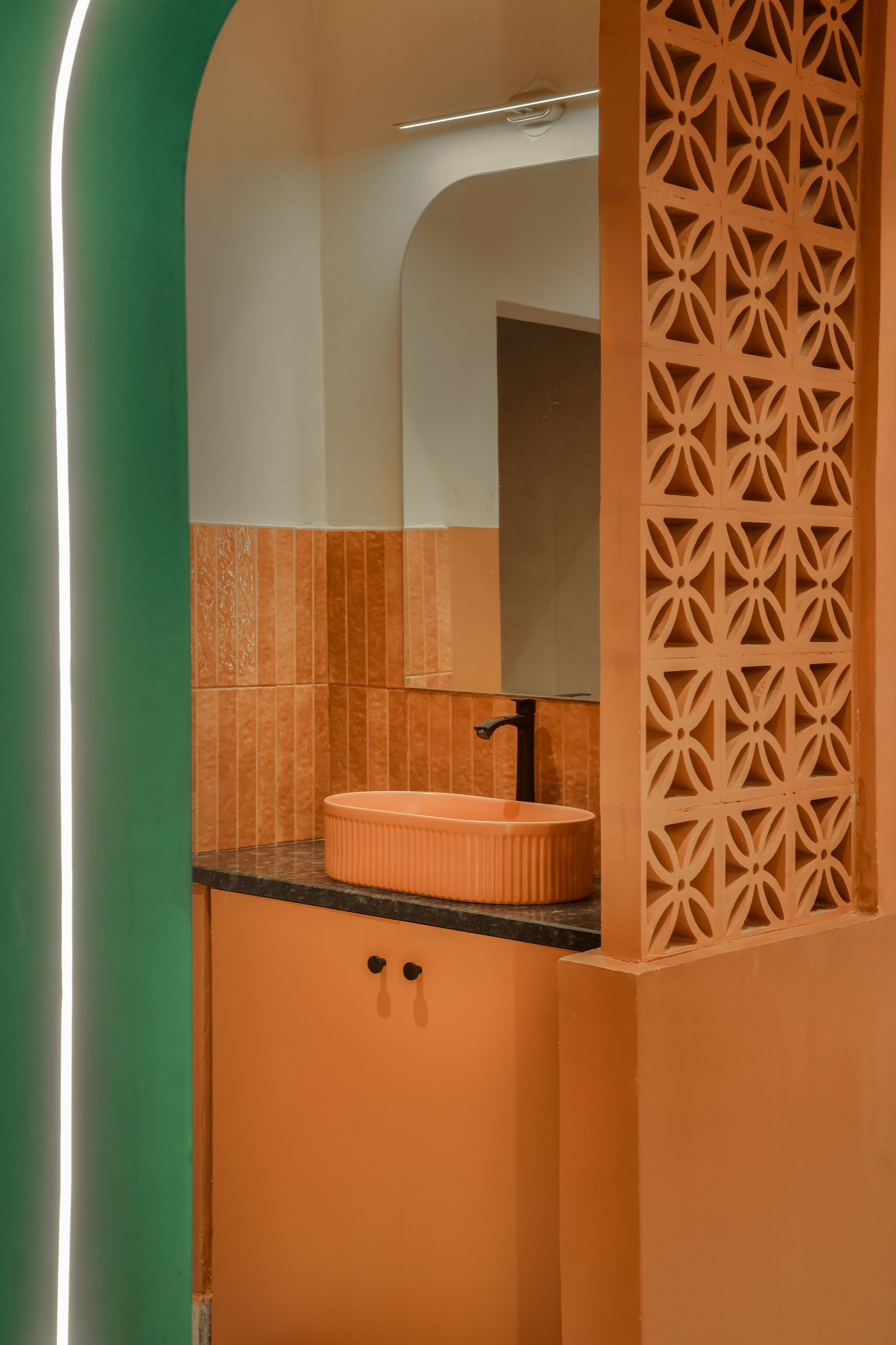 The washroom, where the project's language carries through to a fluted orange basin and a full-height jali screen