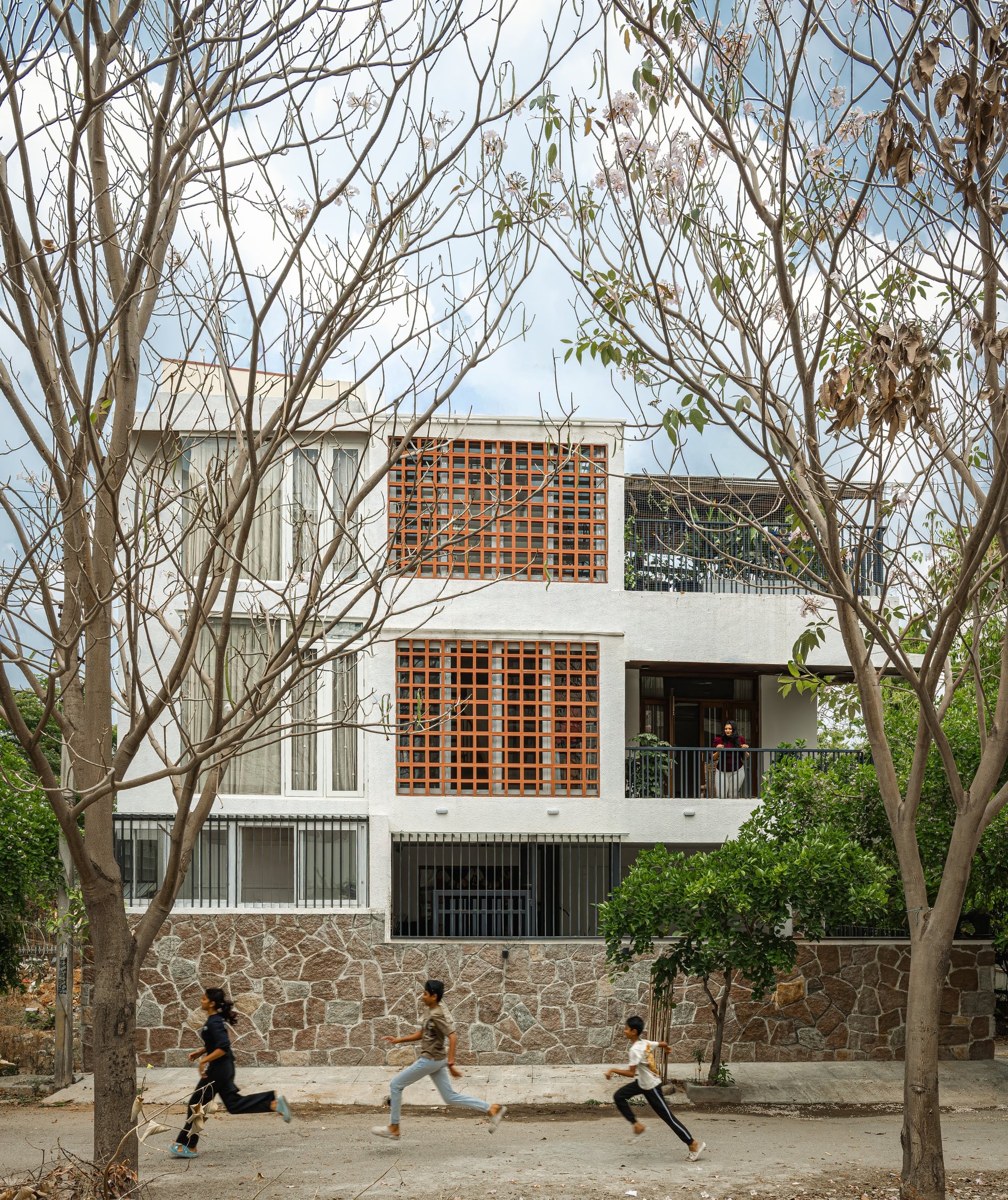 The street elevation: a rubble stone plinth, a white stucco mass and two brick jali panels filtering light into the bedrooms