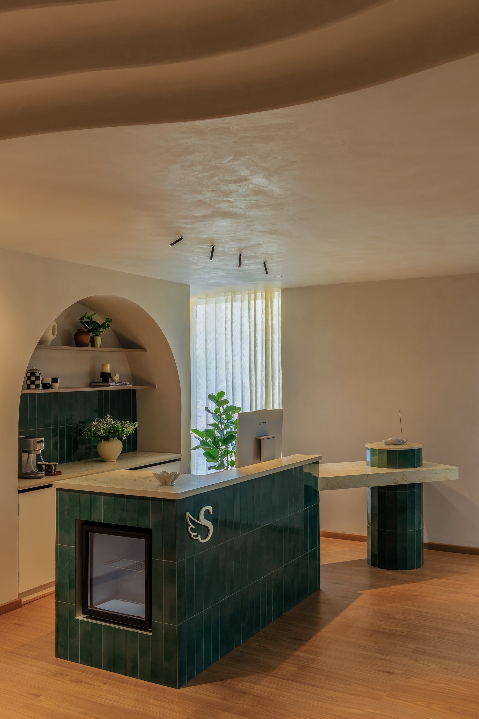 The reception counter in stacked emerald tiles, topped with warm cream stone