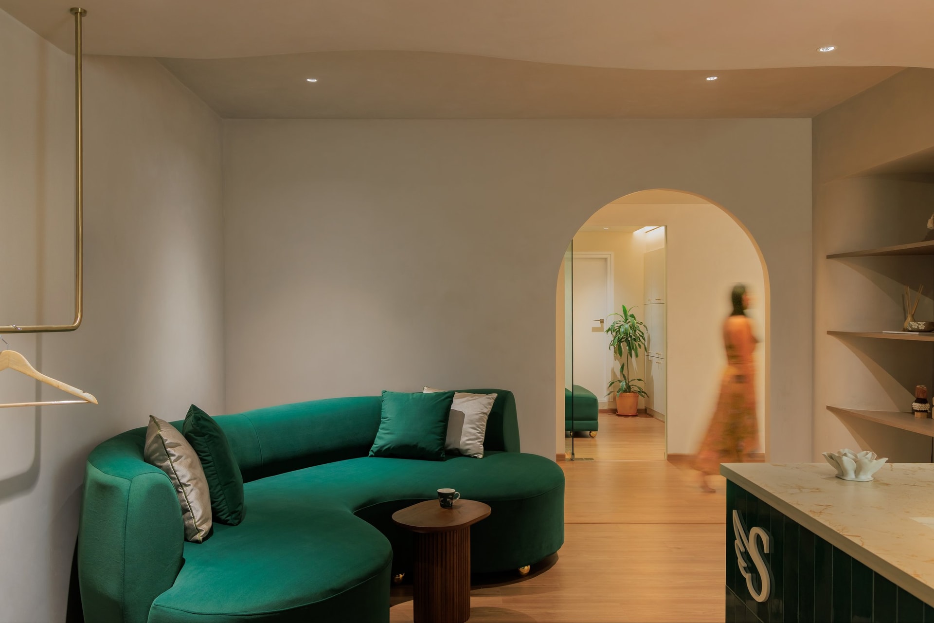 The waiting lounge, anchored by a curved emerald sofa and a slim brass rail