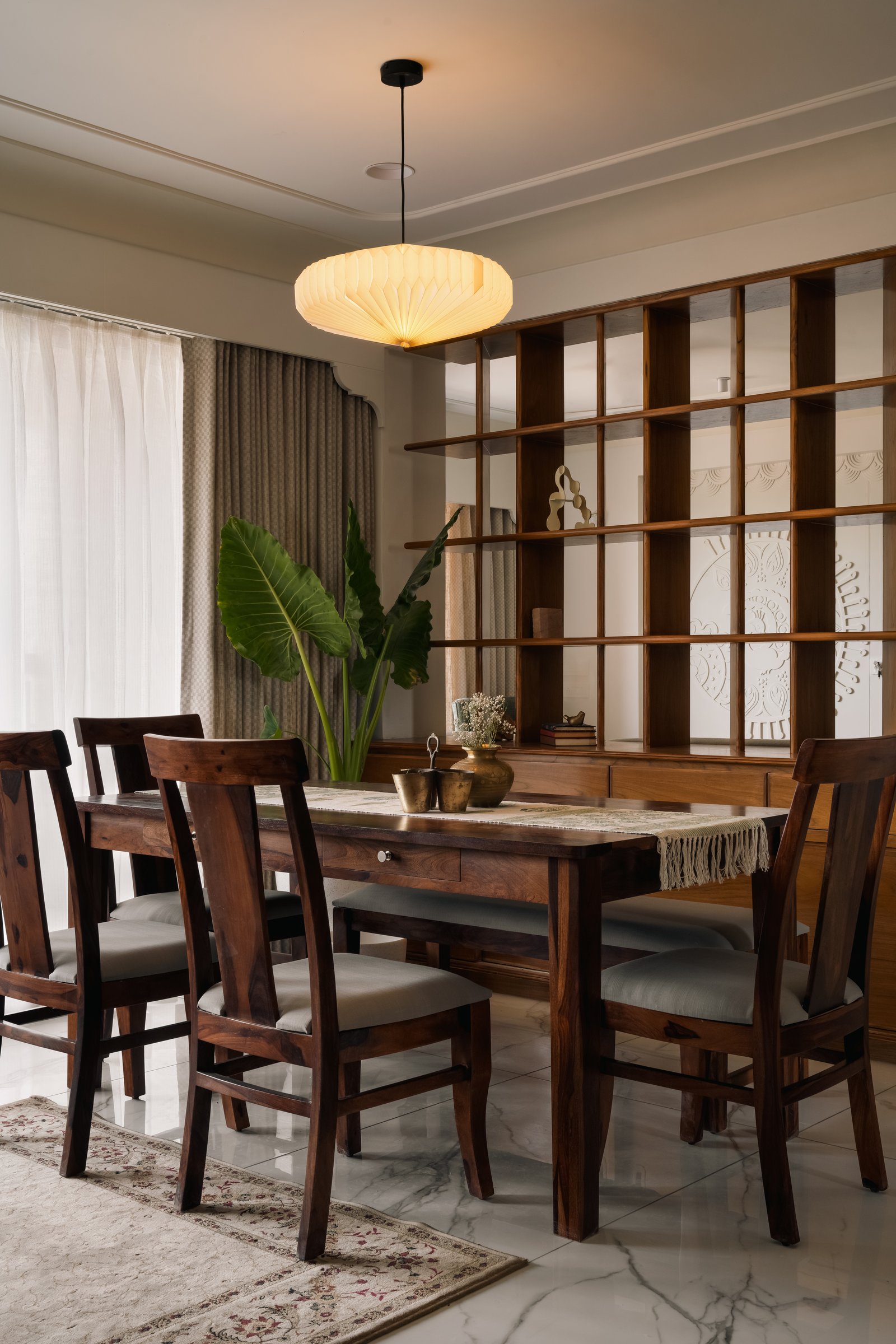The dining area, where a dark wood table and a pleated pendant sit against a second wood-framed grid