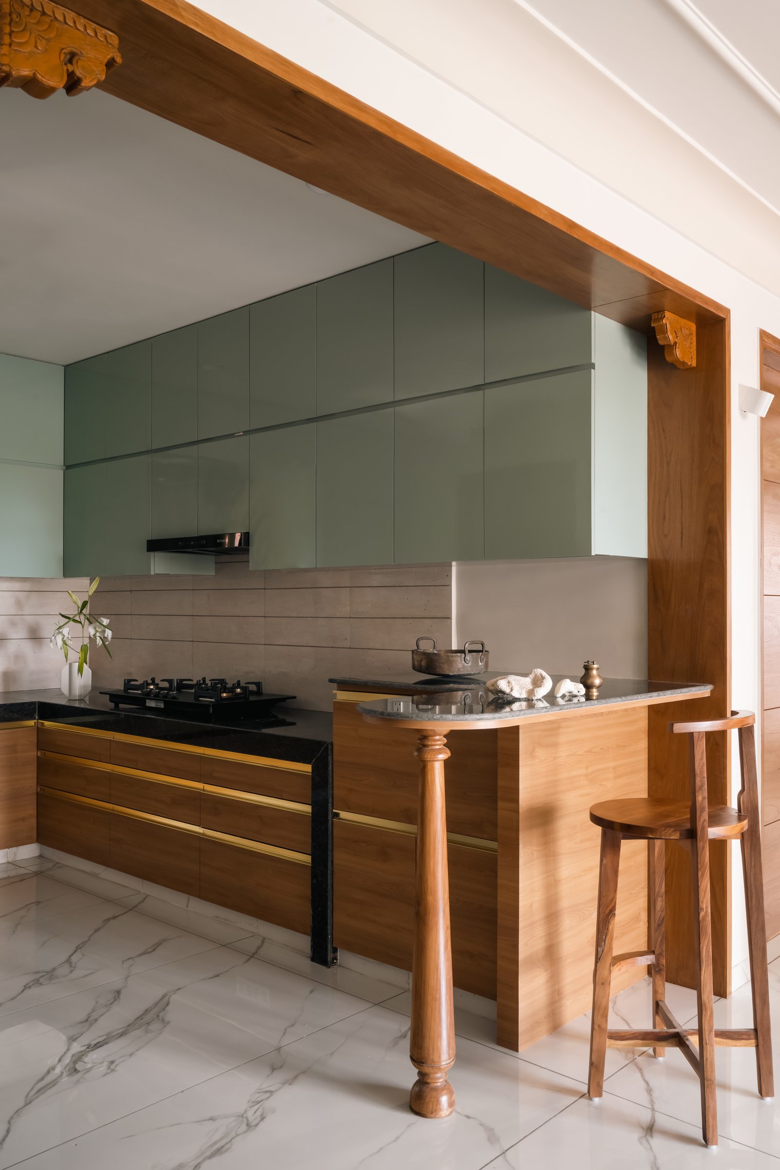 The kitchen, where sage cabinetry meets warm wood lowers with brass inlay and a turned wooden post