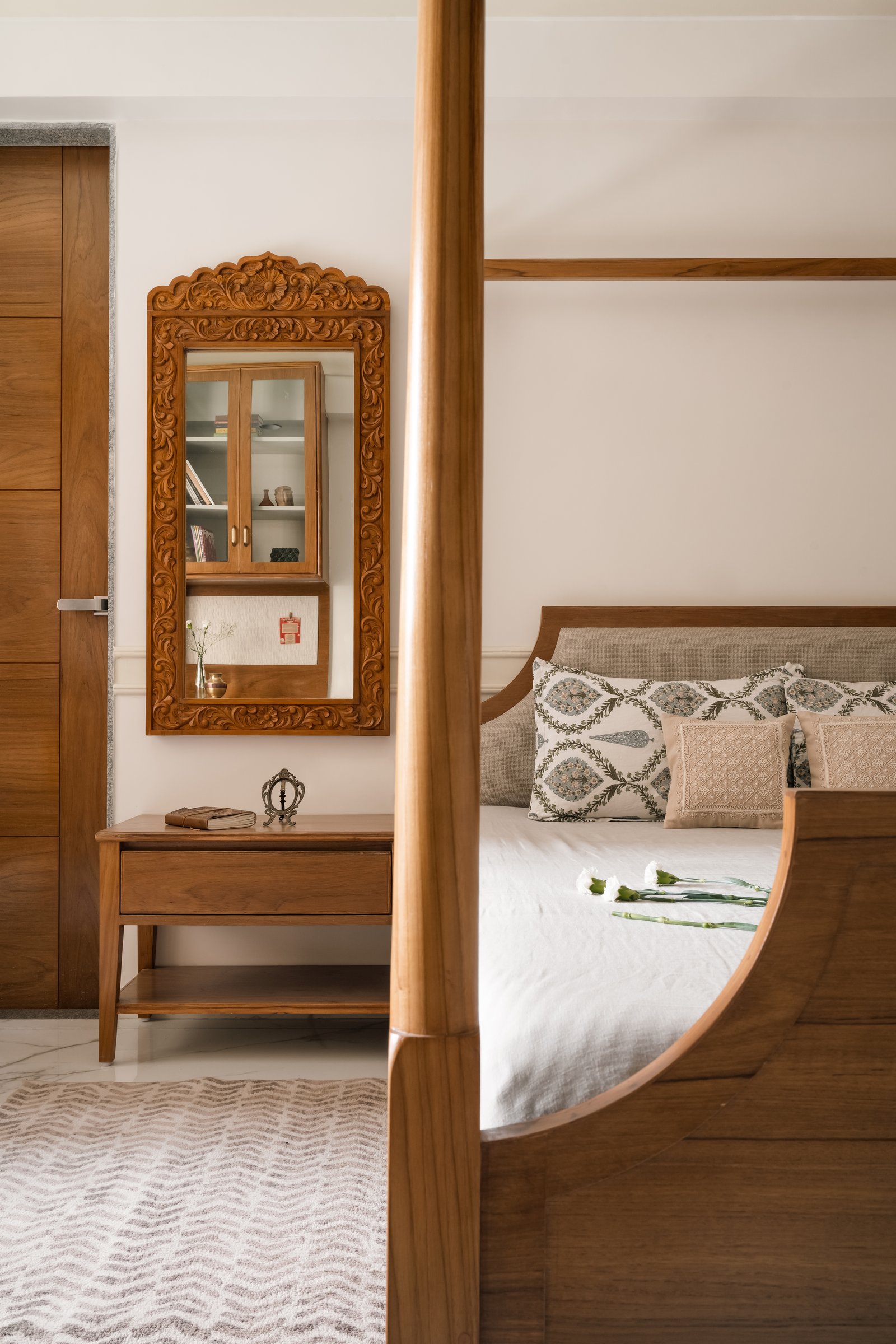 A closer view of the bedroom, where a carved mirror and block-printed cushions extend the home’s craft register