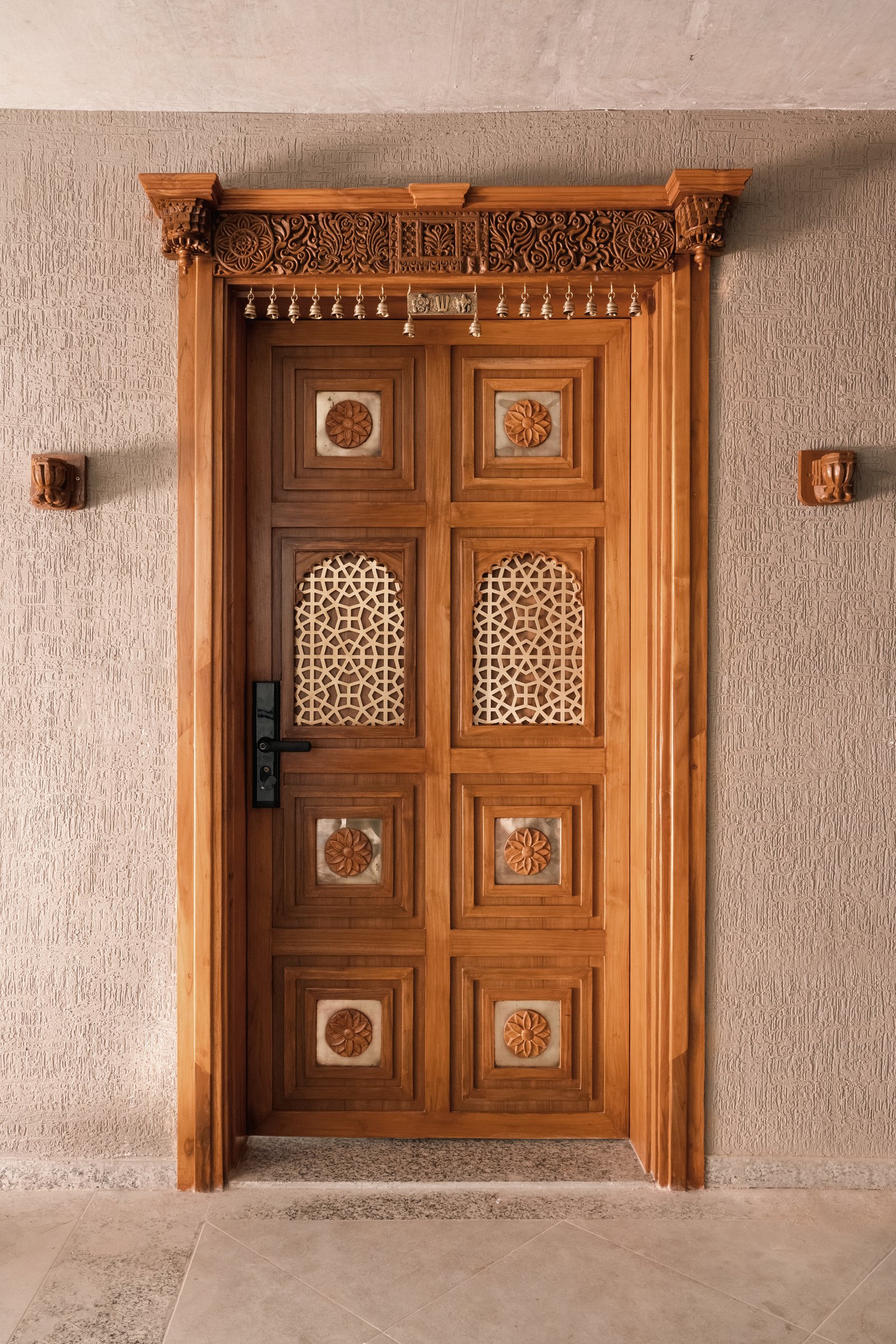 The entry door, where carved teak, jaali inserts, and a beaded lintel establish the home’s craft vocabulary