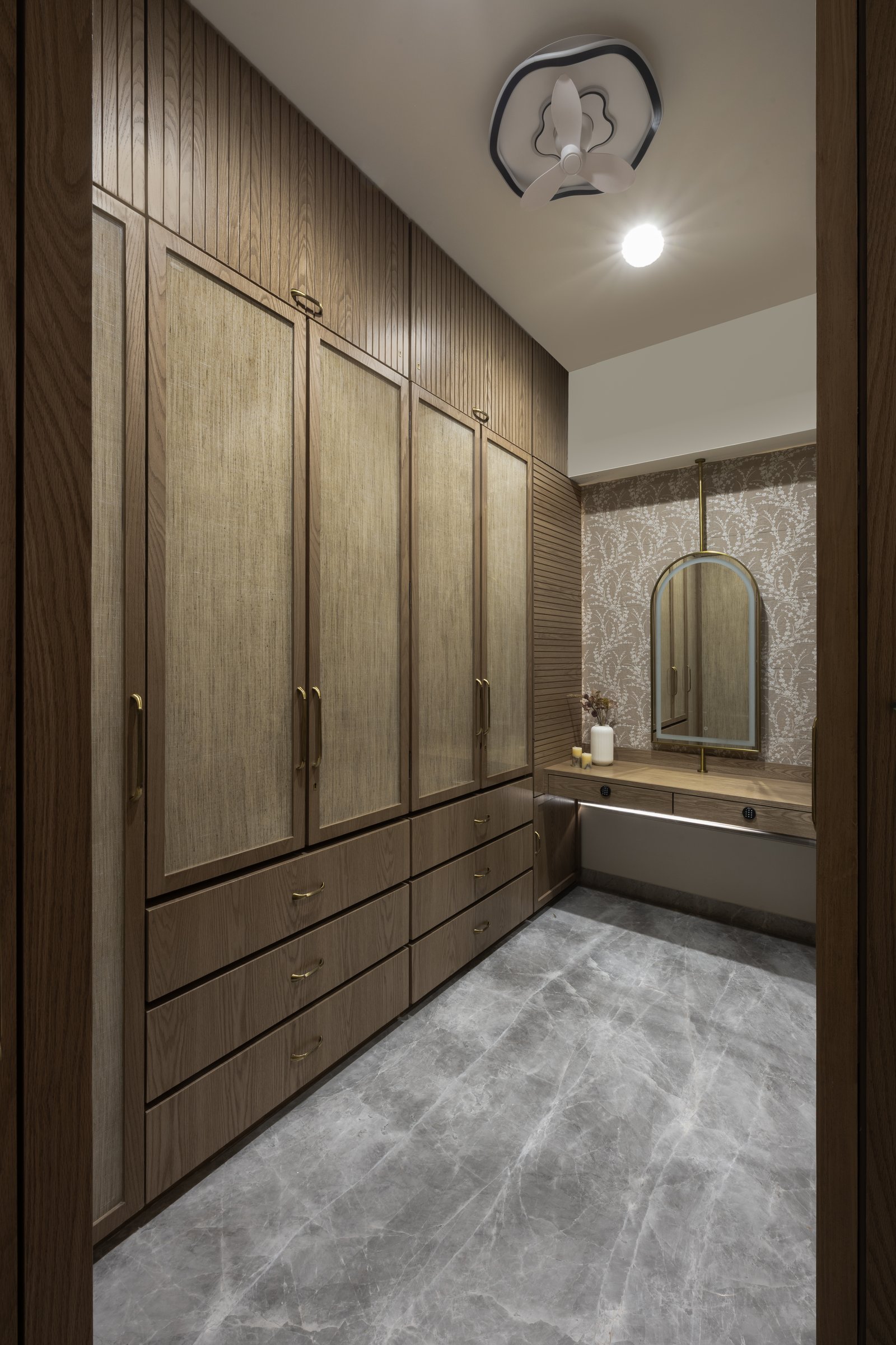 The master walk-in: floor-to-ceiling fluted and grained wood, brass pulls, and an arched mirror above the dressing counter