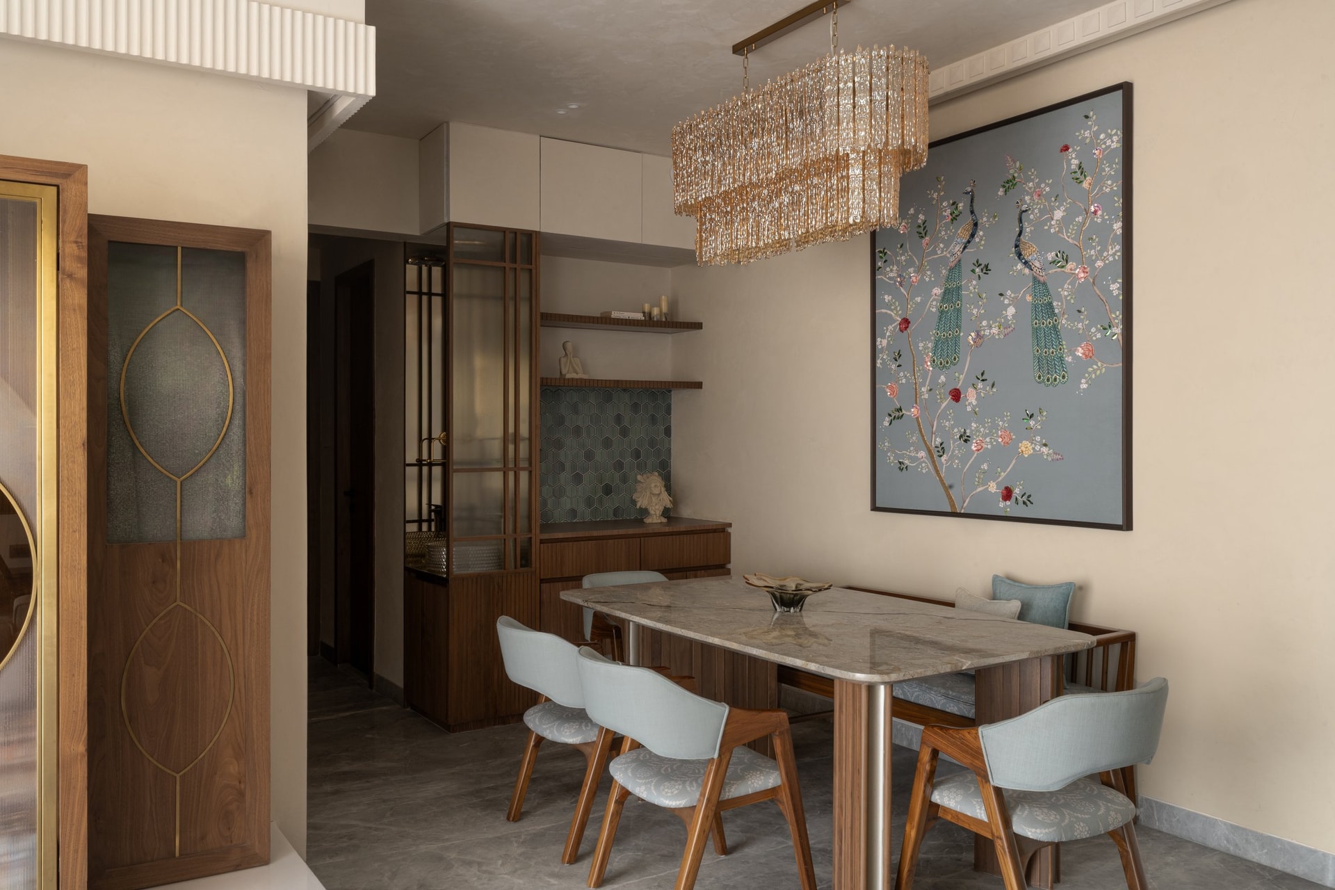 The dining zone gathers beneath a long crystal chandelier, the peacock artwork its emotional anchor