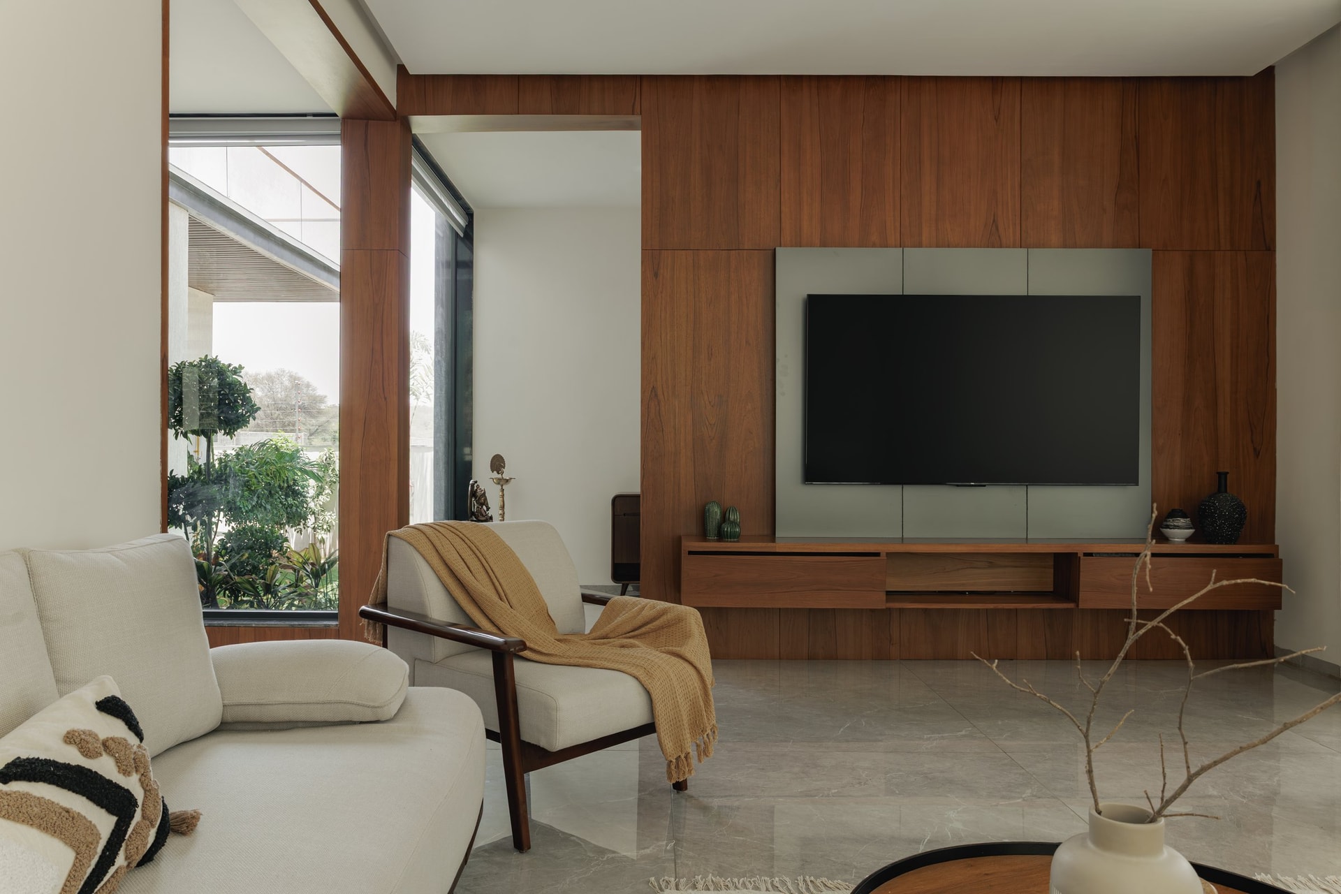 The wood-clad living-room wall, where vertical panelling and a floating media console anchor the room against a side window onto the garden