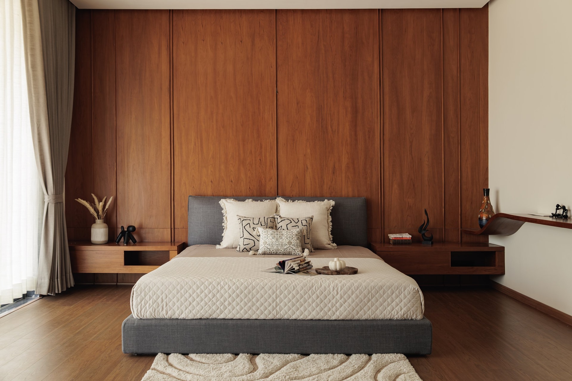 The master bedroom, organised around a tall panelled wood wall and a low grey upholstered bed