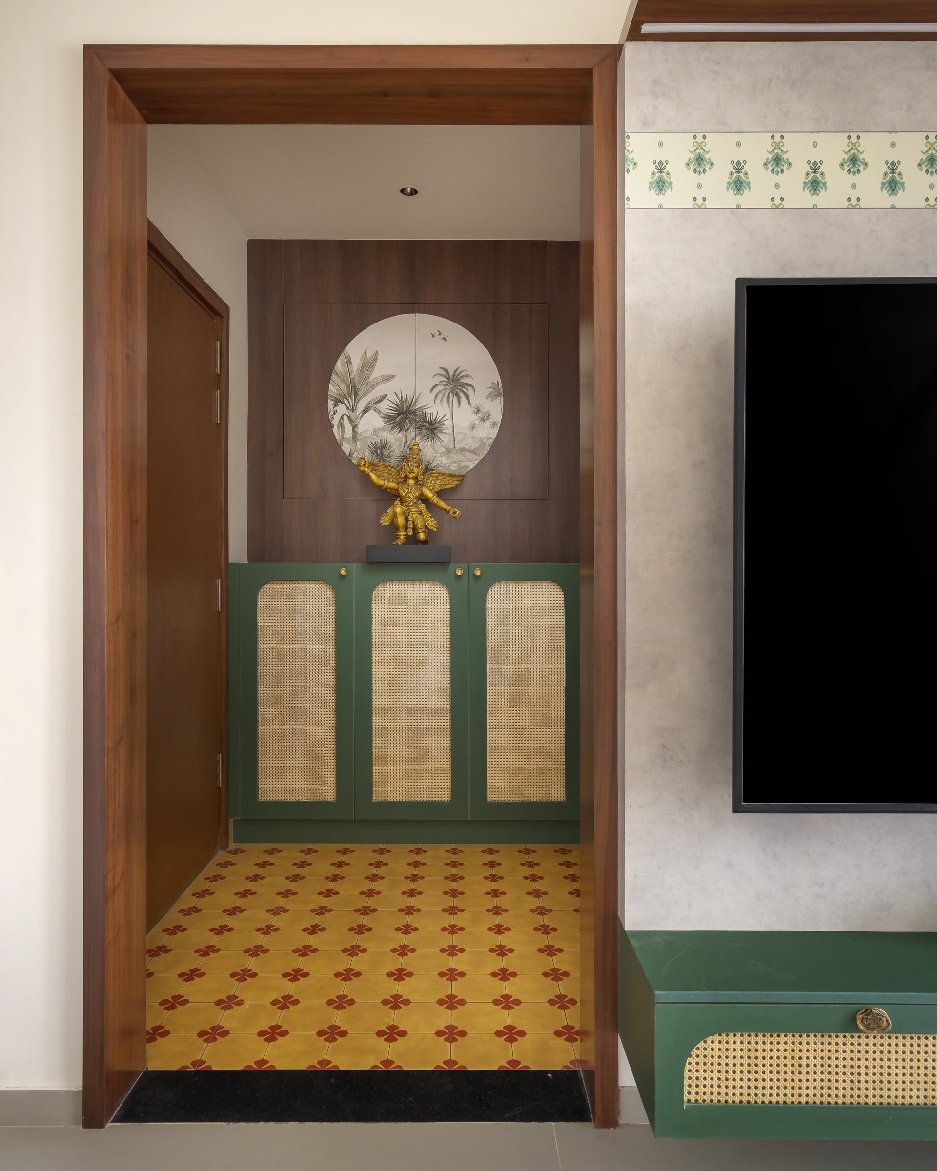 The foyer, where a patterned cement tile floor and a cane-panelled green cabinet establish the home's material grammar at once
