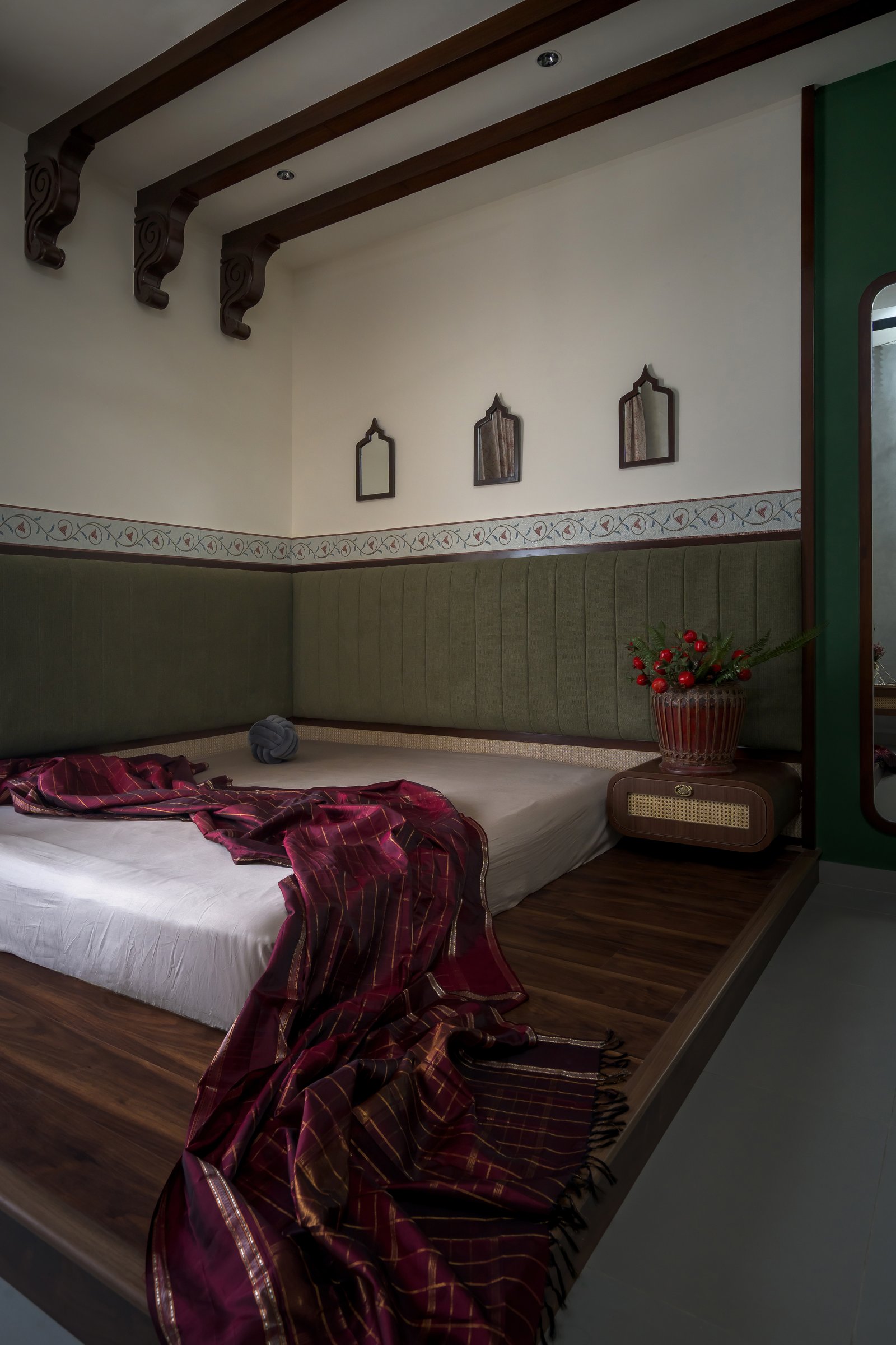 The master bedroom, where exposed wooden rafters and carved brackets reinterpret the Chettinad roof language above a platform bed