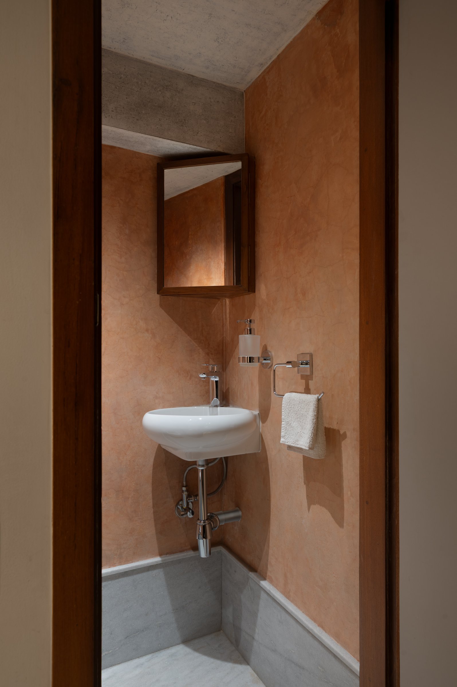 The washroom, finished in warm terracotta-toned plaster with a stone dado and a compact timber-framed mirror cabinet