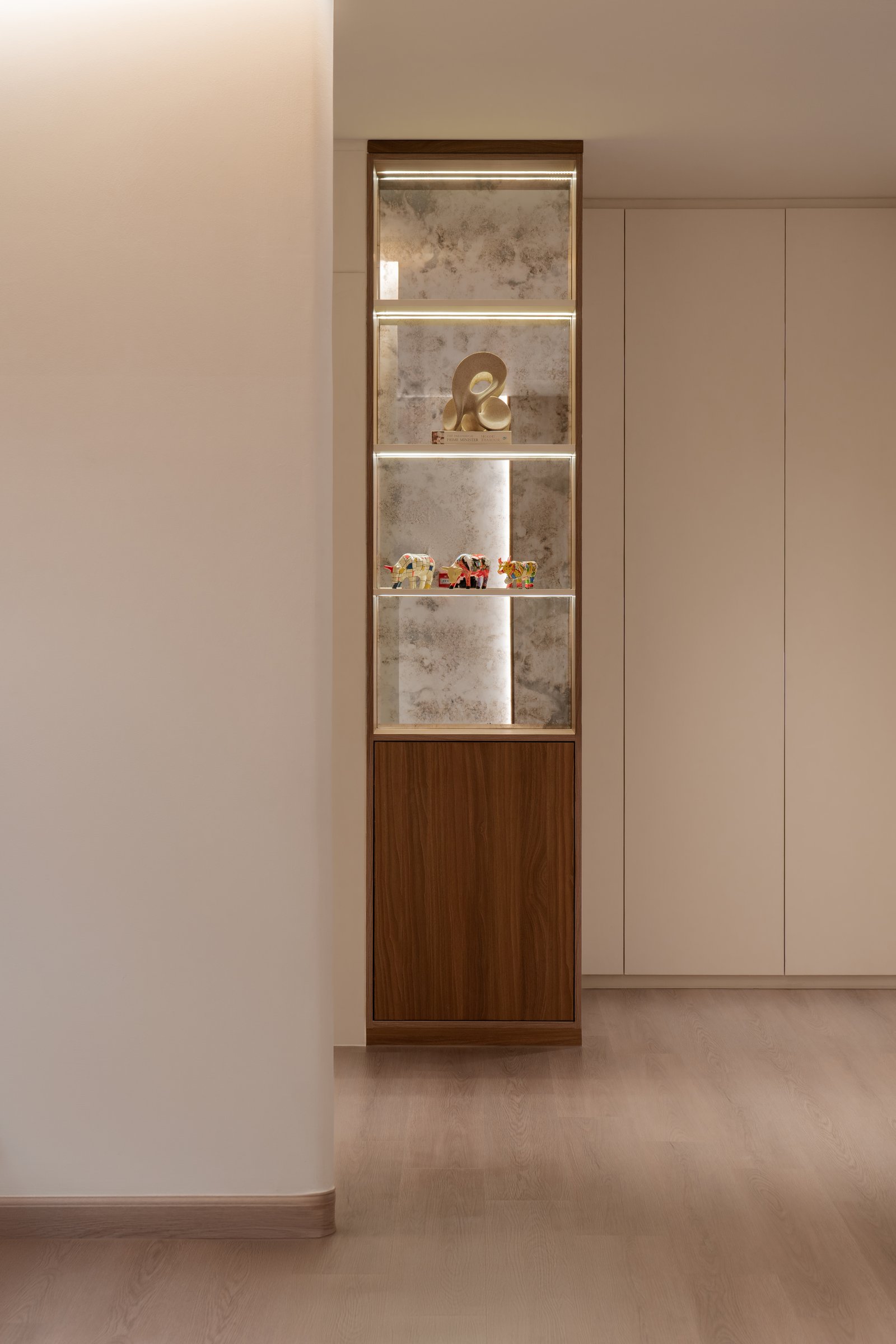 A corridor display niche, where a sculptural award and hand-painted figures sit against a backlit antiqued mirror