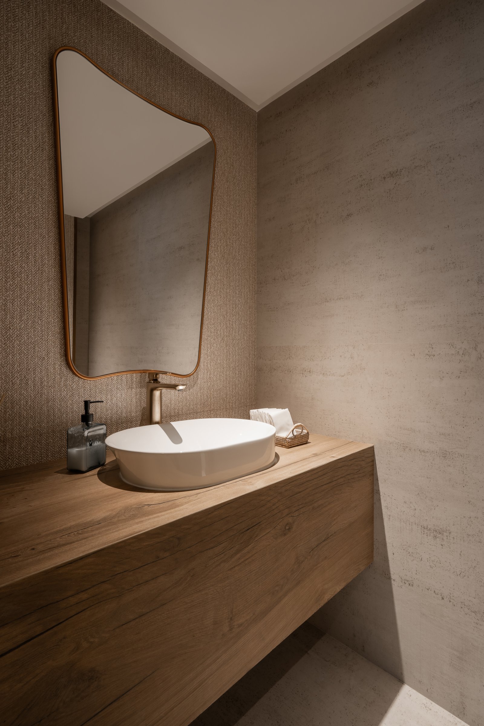 The powder room, where a thick timber counter, a vessel basin, and a softly curved mirror share a single quiet register
