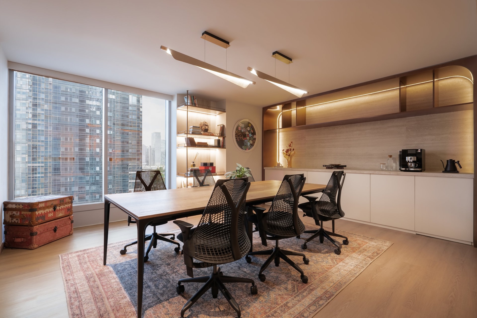 The principal meeting room, where a wood conference table, a linear pendant, and a travertine coffee counter share a single warm register