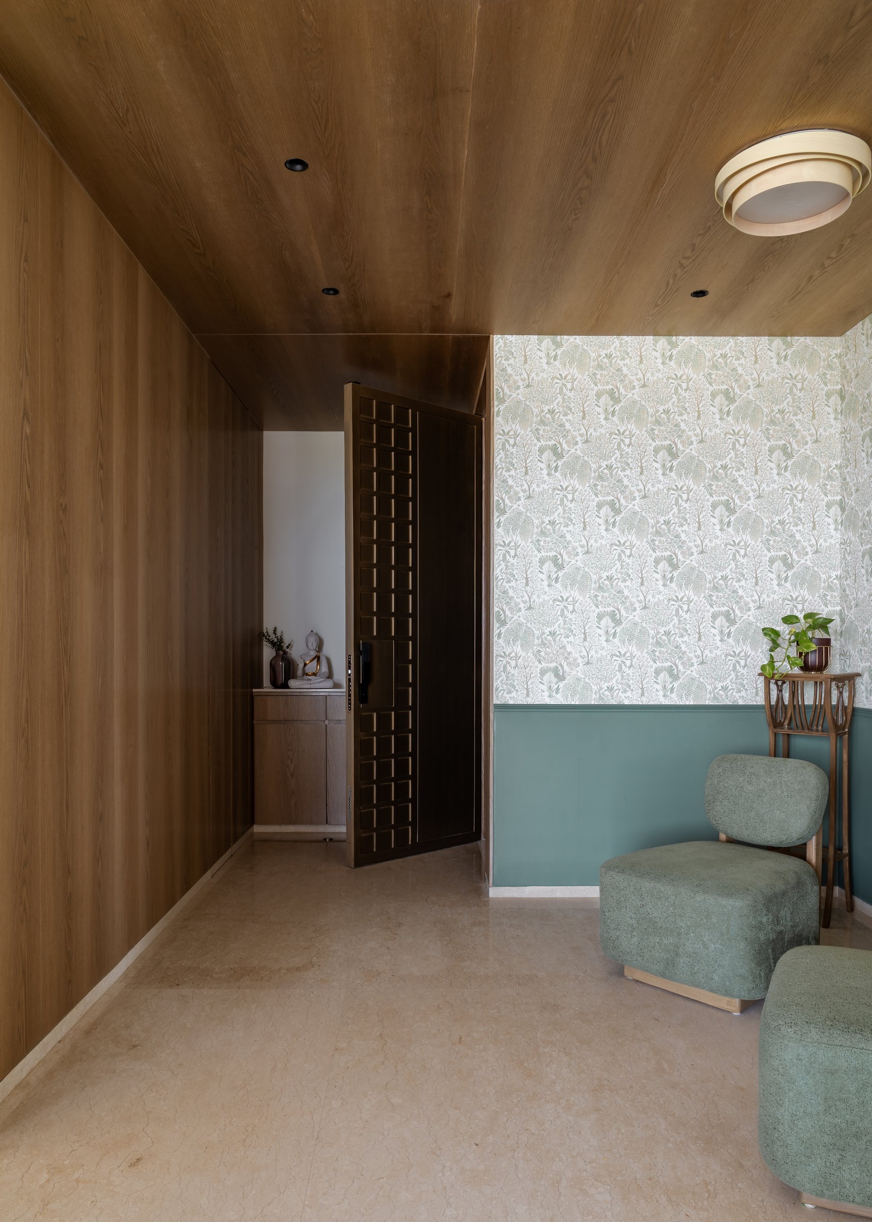 The foyer, where a ribbed oak ceiling meets a sage botanical wallpaper and a teal wainscoted dado